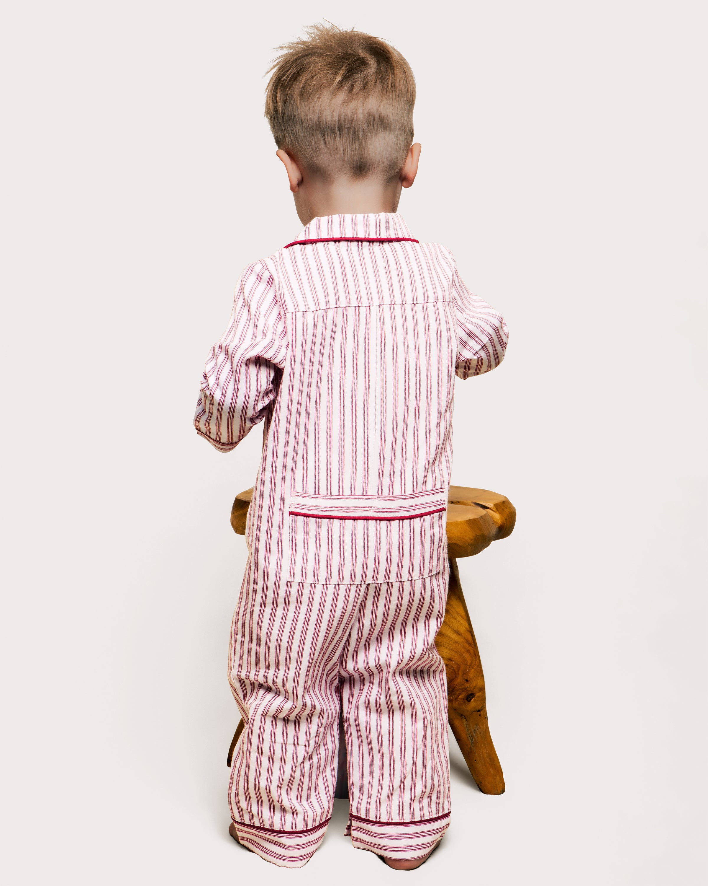 The Babys Twill Romper in Antique Red Ticking by Petite Plume is a childs long-sleeve jumpsuit with vertical red and white stripes, made from lightweight brushed twill. It features a collar, red trim on the cuffs and ankles, and a back flap pocket.
