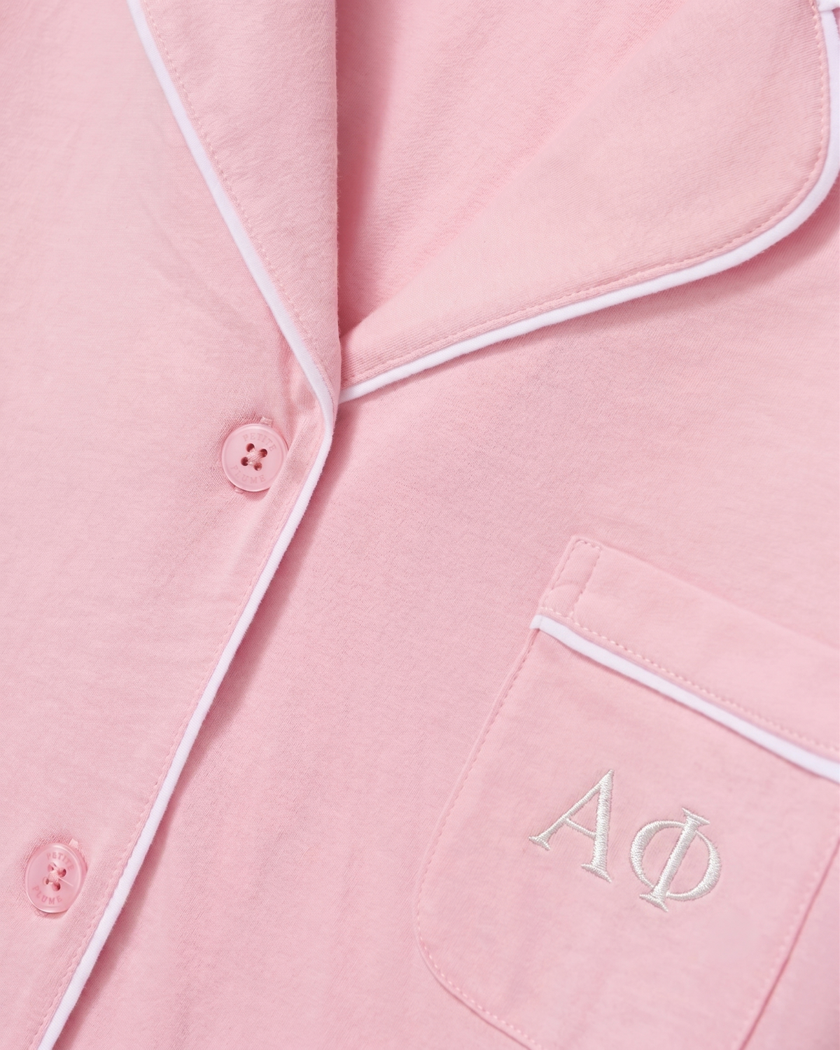 Close-up of the Greek Embroidered Poppy Lightweight Pima Short Set in Pink, featuring a light pink pajama top with white piping, pink buttons, and white embroidered Greek letters ΑΦ on the chest pocket.
