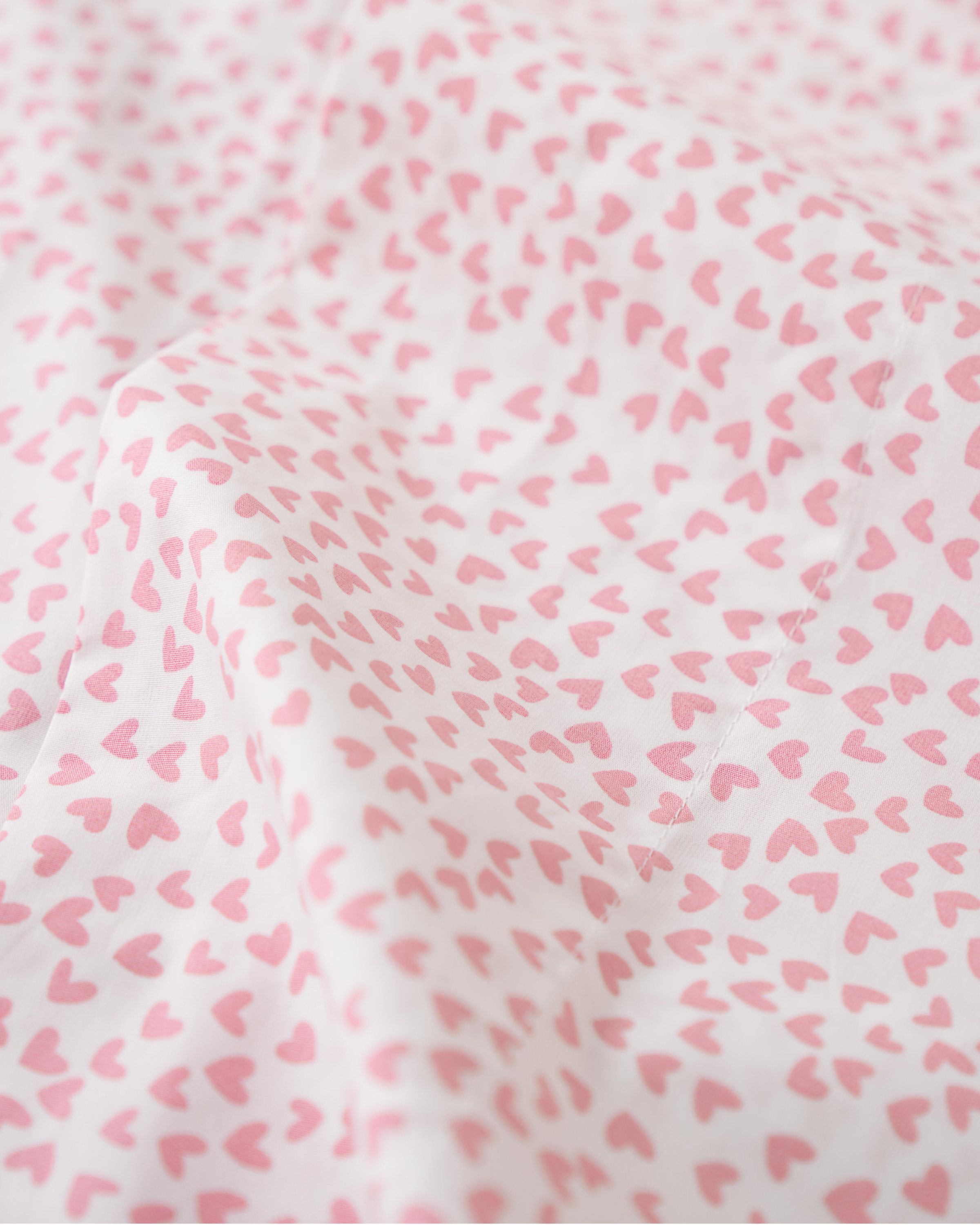 A close-up of Petite Plumes Luxe Premium Cotton Sweethearts Bed Sheets reveals a white fabric made from long-staple cotton, embellished with small pink hearts. These luxury sheets have a slightly wrinkled texture, forming gentle folds that enhance their allure.