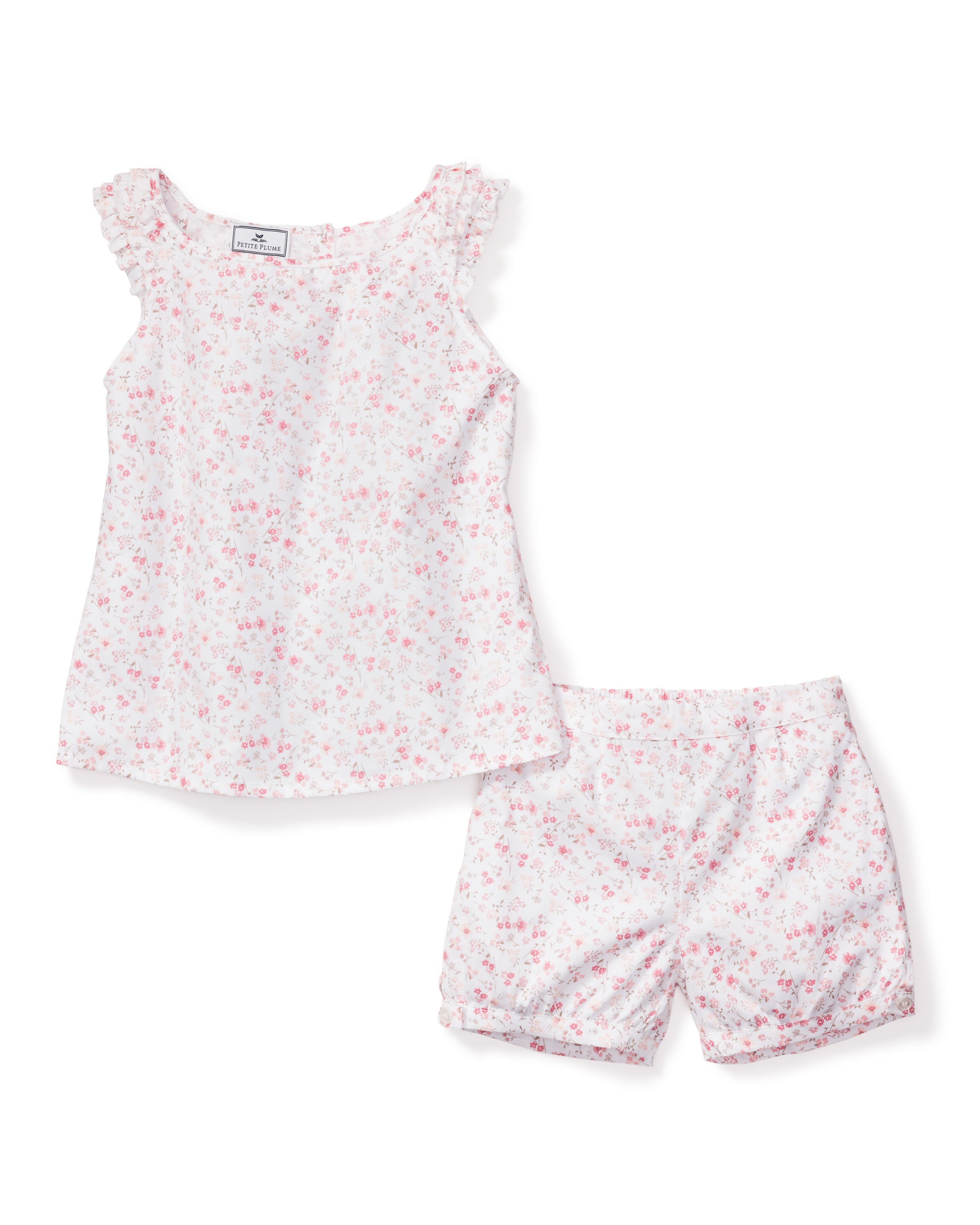 The Girls Twill Amelie Short Set in Dorset Floral by Petite Plume is a cotton pajama set with a sleeveless top and shorts, featuring white fabric adorned with delicate pink flower buds and ruffled shoulder accents for a feminine touch.