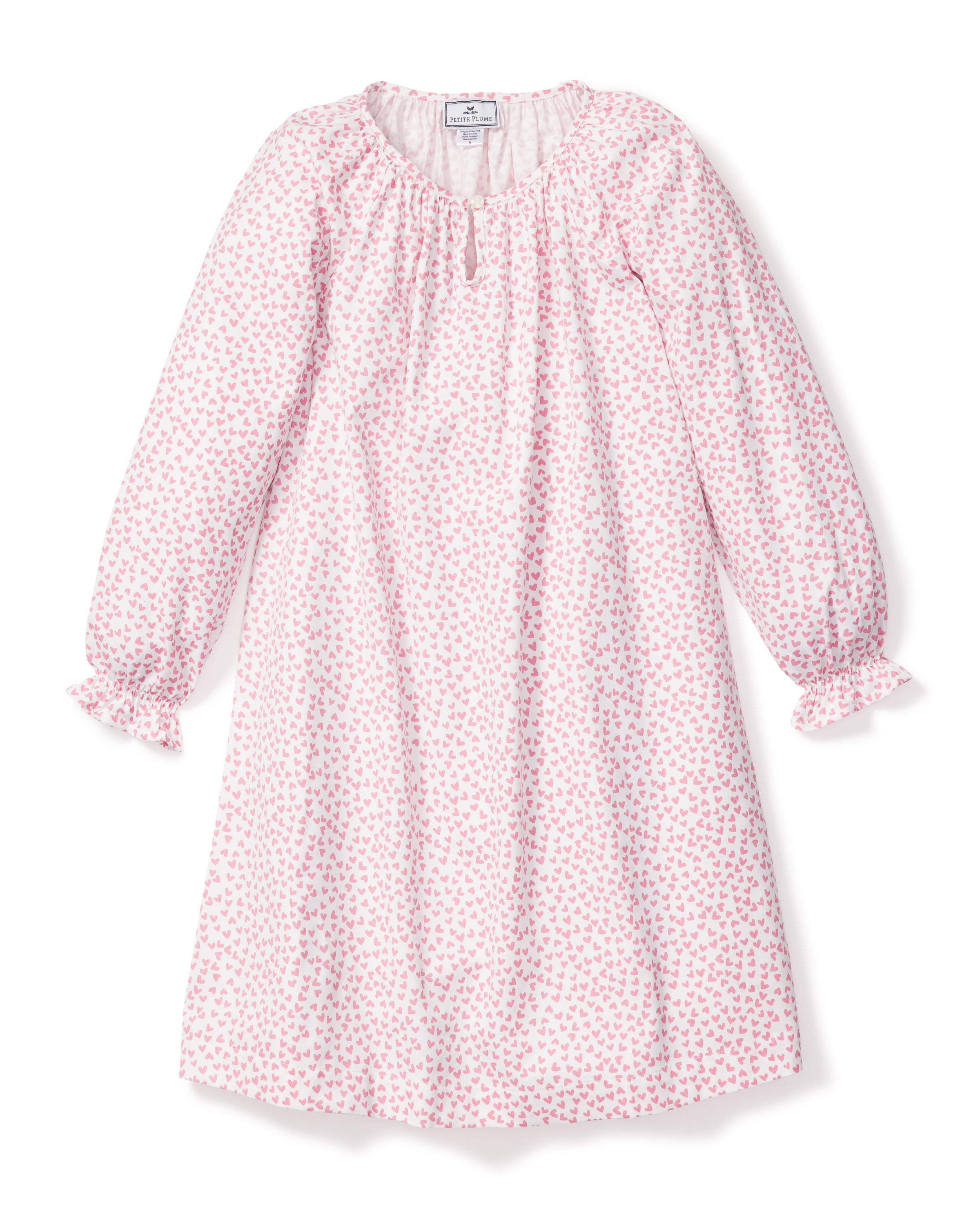 The Girls Twill Delphine Nightgown in Sweethearts by Petite Plume features long sleeves, white fabric with a pink floral pattern, is made from yarn-dyed cotton, and has a ruffled neckline with a small bow and ruffled sleeve cuffs.