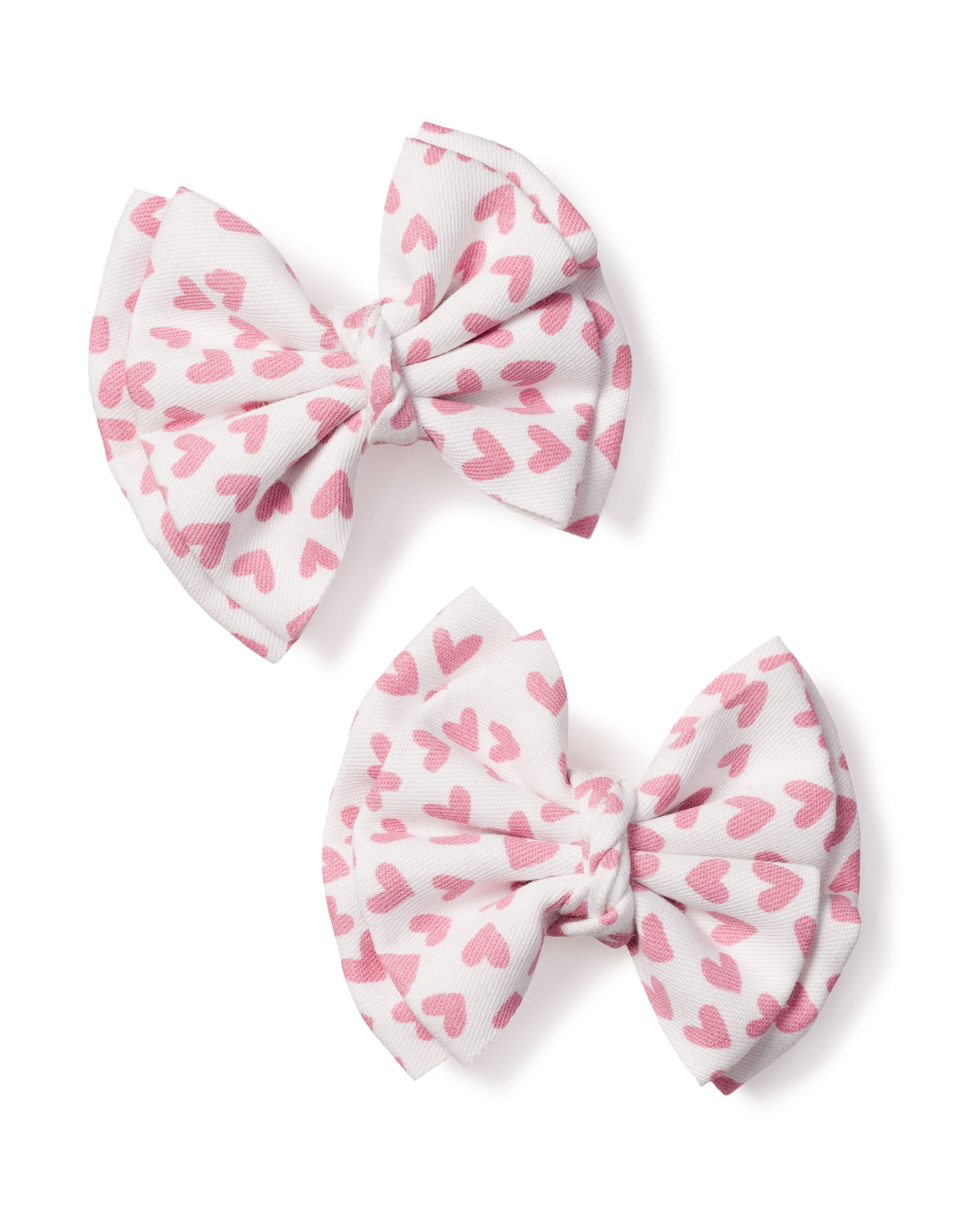 Two Petite Plume Girls Hair Bows in Sweethearts, featuring white fabric with pink heart patterns, are arranged diagonally on a plain white background. These festive bows are perfect as a holiday gift or charming stocking stuffer.
