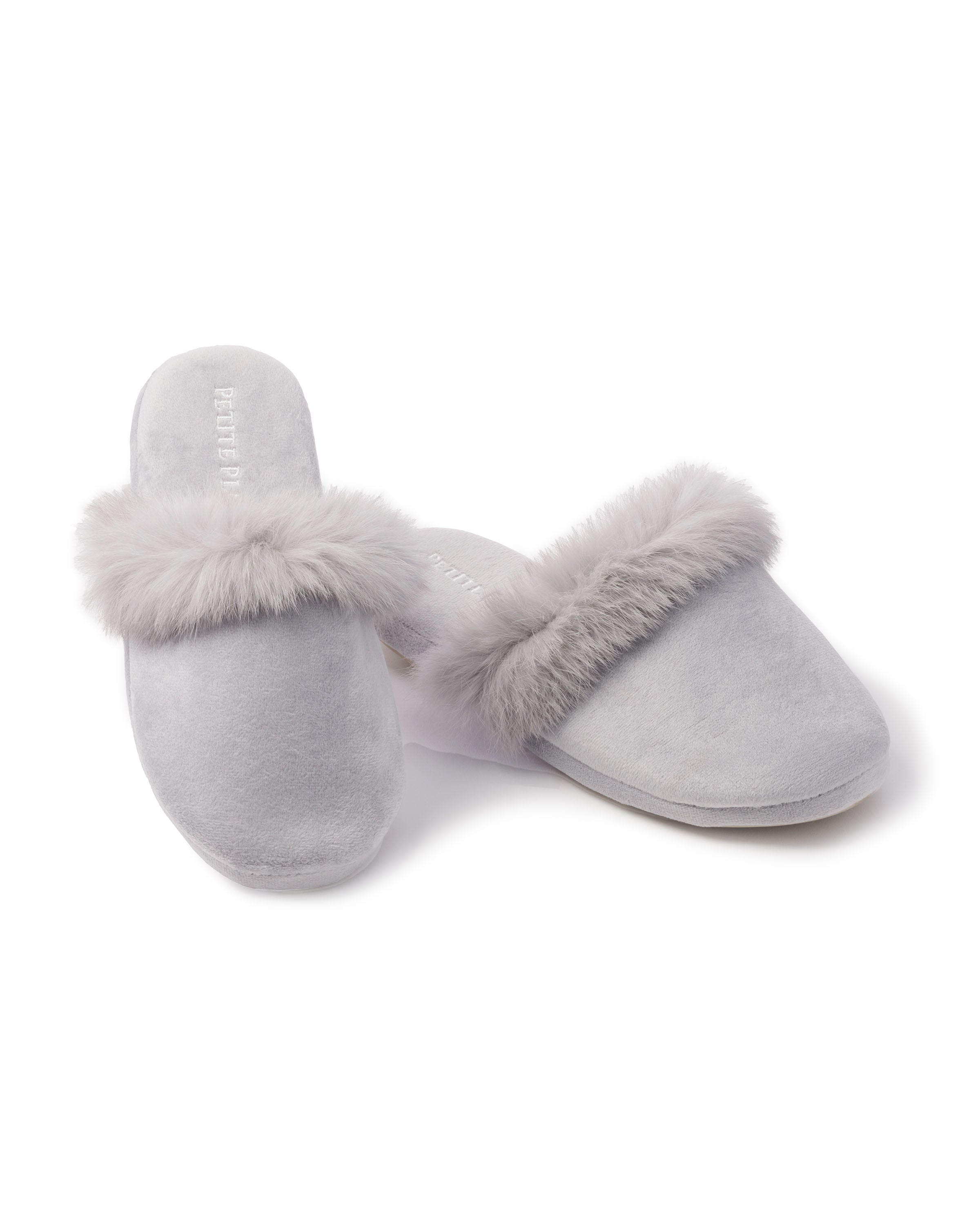 A pair of Womens Faux Fur Trim Slippers in light gray by Petite Plume, showcasing plush comfort with soft fur trim, is displayed on a white background. One slipper stands upright while the other rests elegantly on its side.