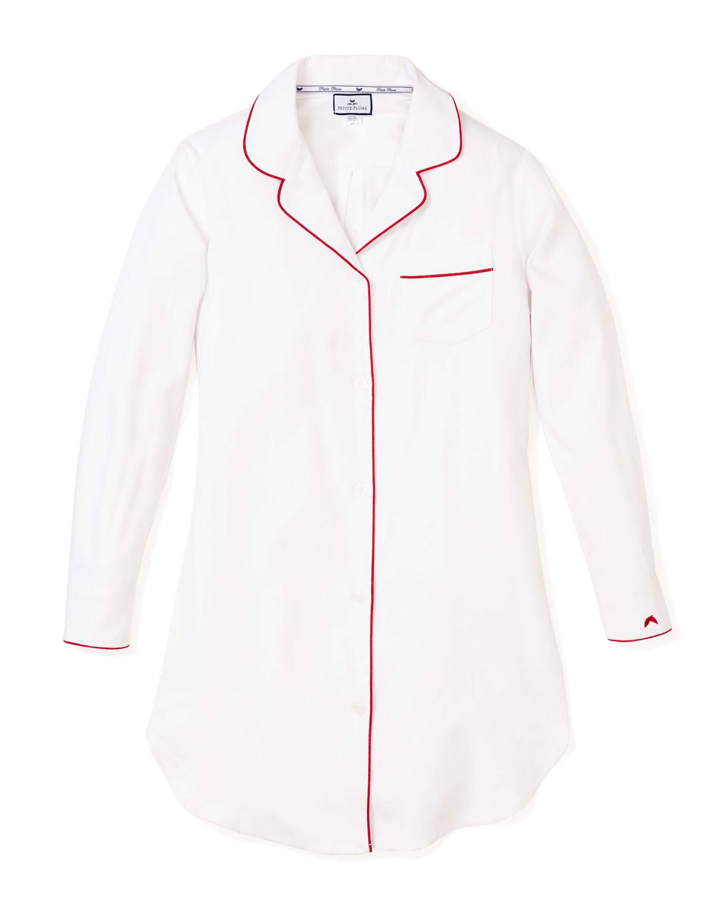 The Womens Twill Nightshirt in White with Red Piping by Petite Plume is a cotton twill button-down sleep shirt with red piping on the collar, cuffs, and chest pocket. It features a single pocket and curved hem for style and comfort throughout restful nights.