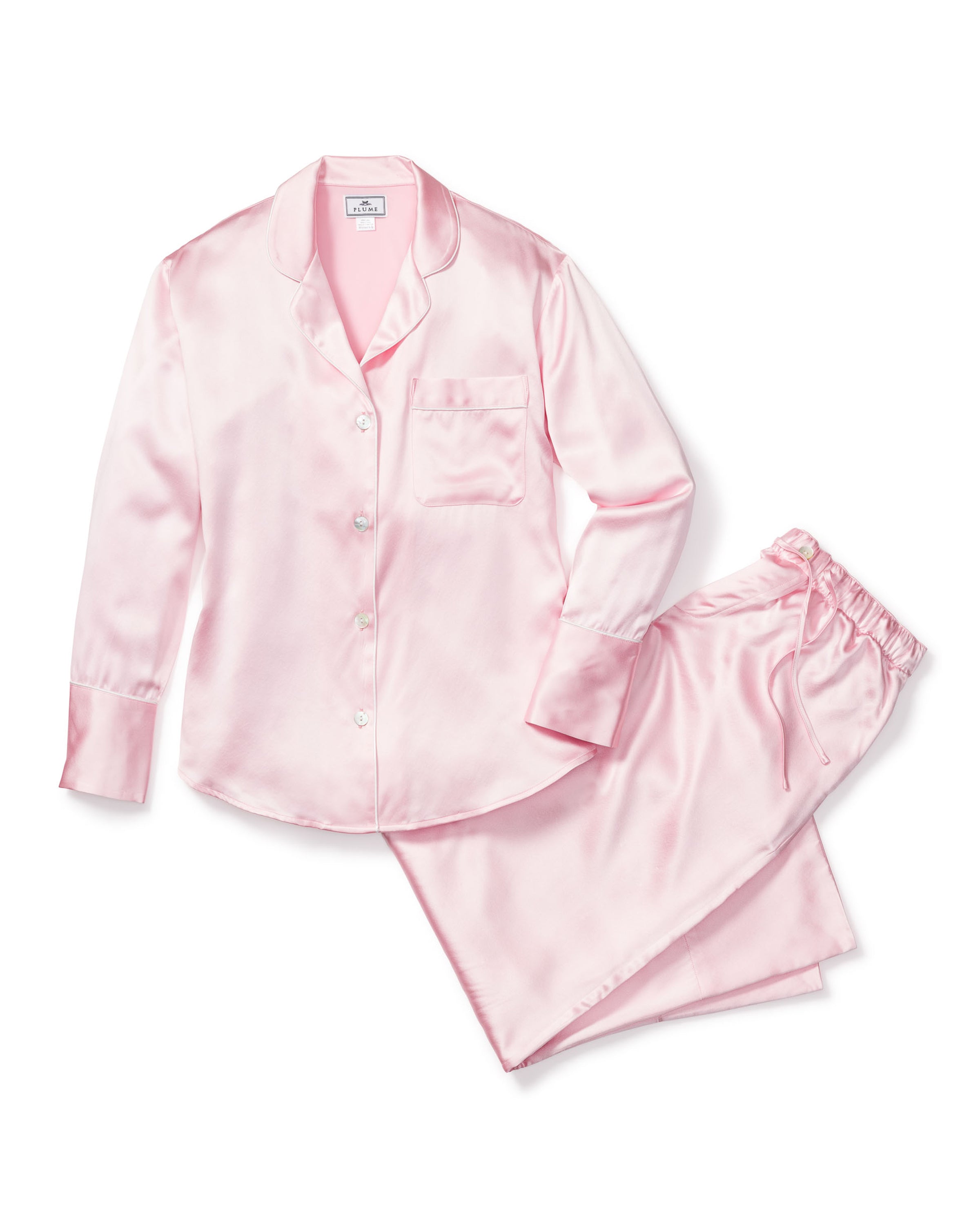 The Womens Silk Pajama Set in Pink by Petite Plume, featuring a long-sleeve button-up shirt with a chest pocket and matching elastic-waistband pants, epitomizes luxury sleepwear as it rests elegantly on a white background.
