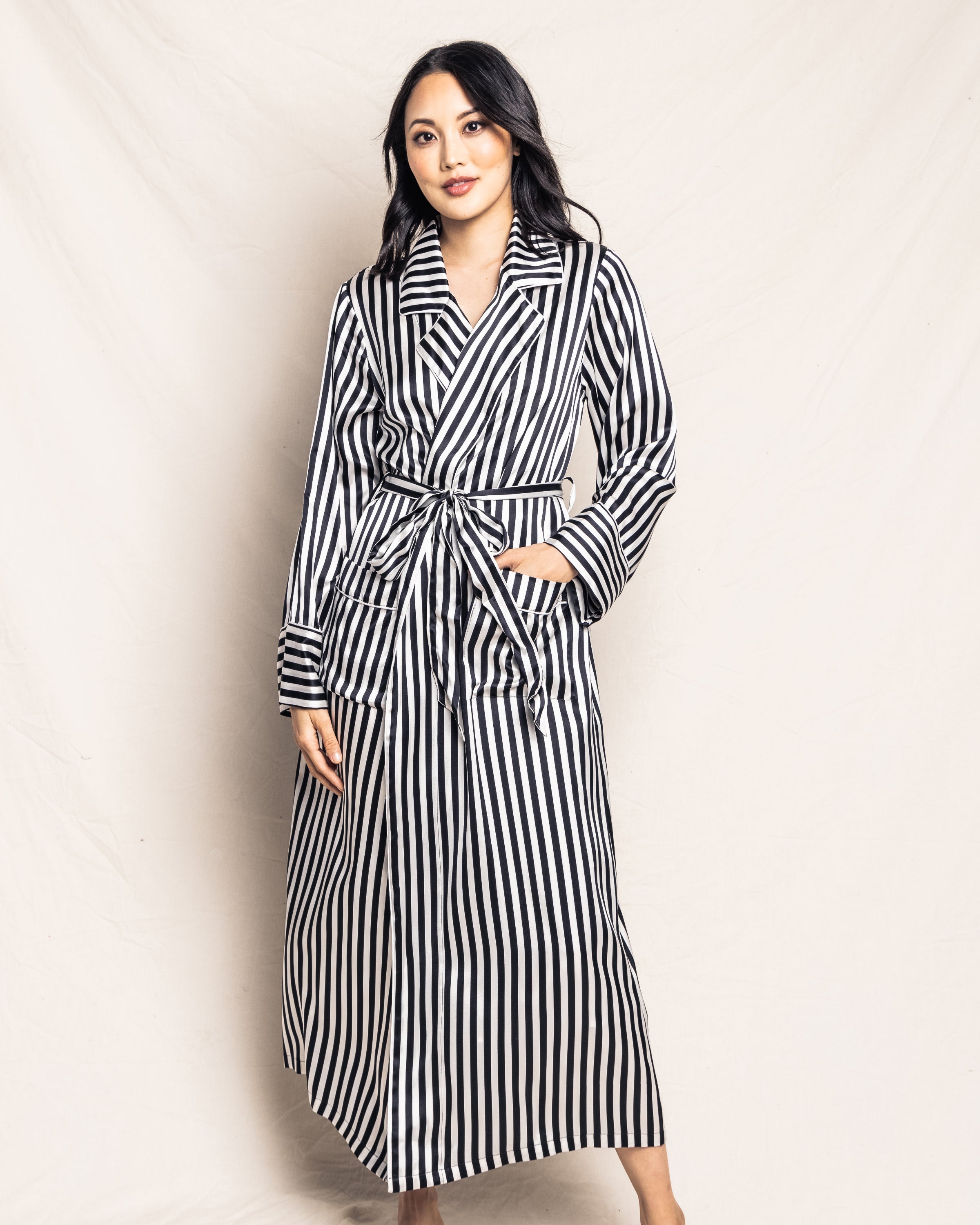 A person in a Petite Plume Womens Silk Long Robe in Bengal Stripe poses confidently against a plain backdrop, their long dark hair and expression capturing the bold flair of the Cabaret Collection.