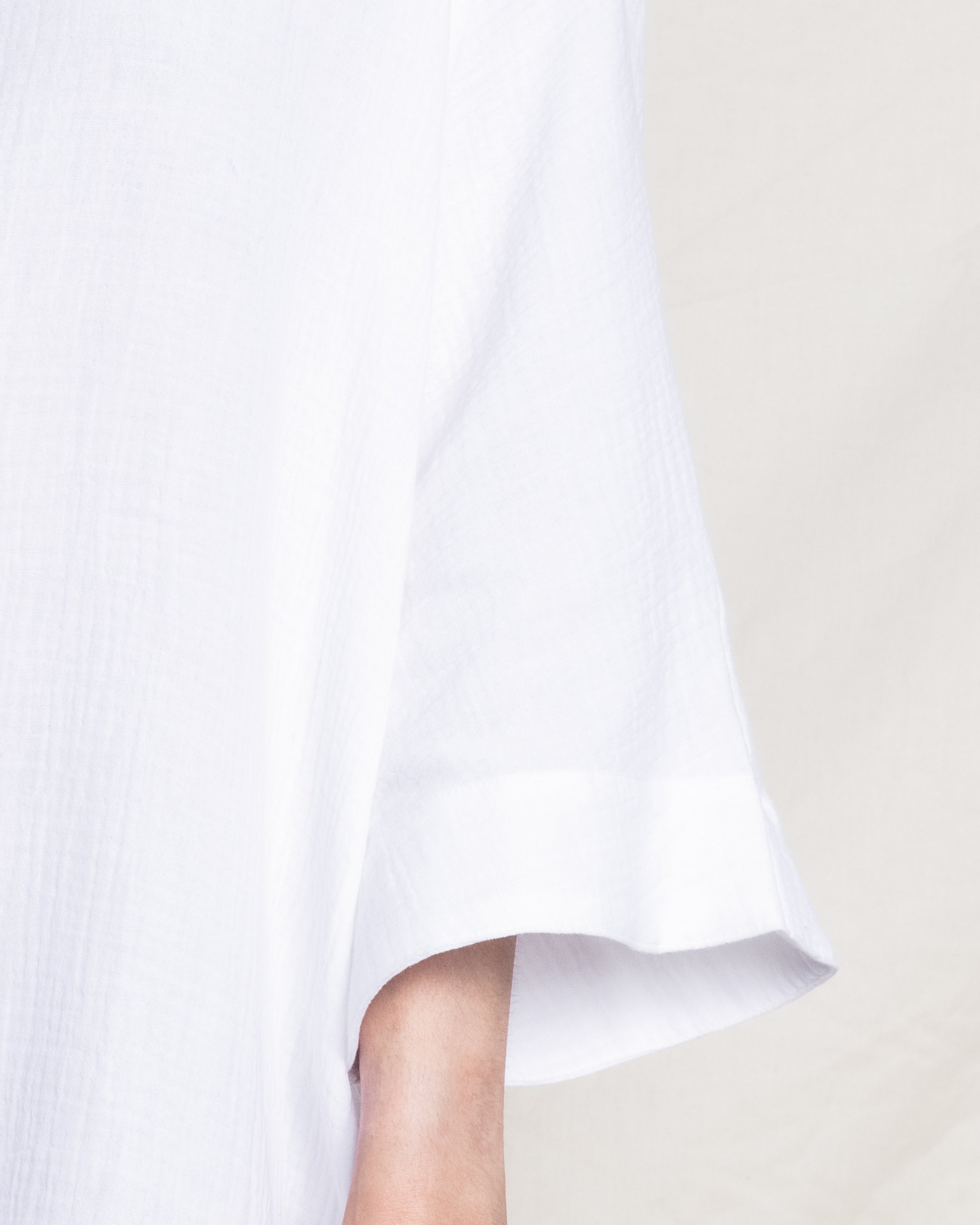A close-up showcases a person wearing Petite Plumes Womens Gauze Short Caftan in White, highlighting the sleeve and upper arm against a light background. The luxurious cotton gauze fabric captures refined comfort.