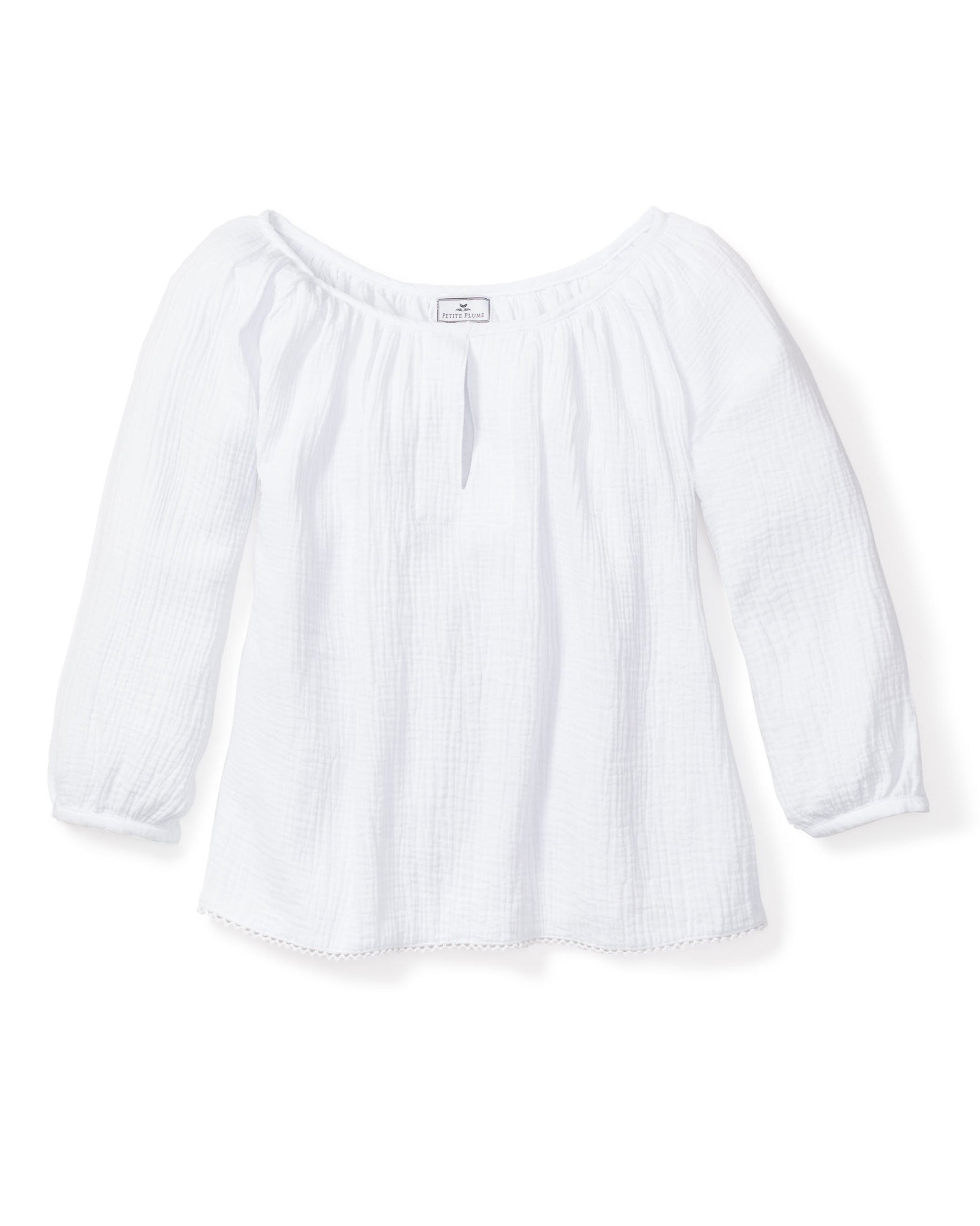 Petite Plumes Womens Gauze Willow Scoopneck Top in White is a long-sleeve peasant blouse made from luxury cotton gauze, with a scooped neckline and vertical texture. It is light and airy, forming a flowing blouson silhouette with simple hem and cuffs, plus a small label near the neckline.