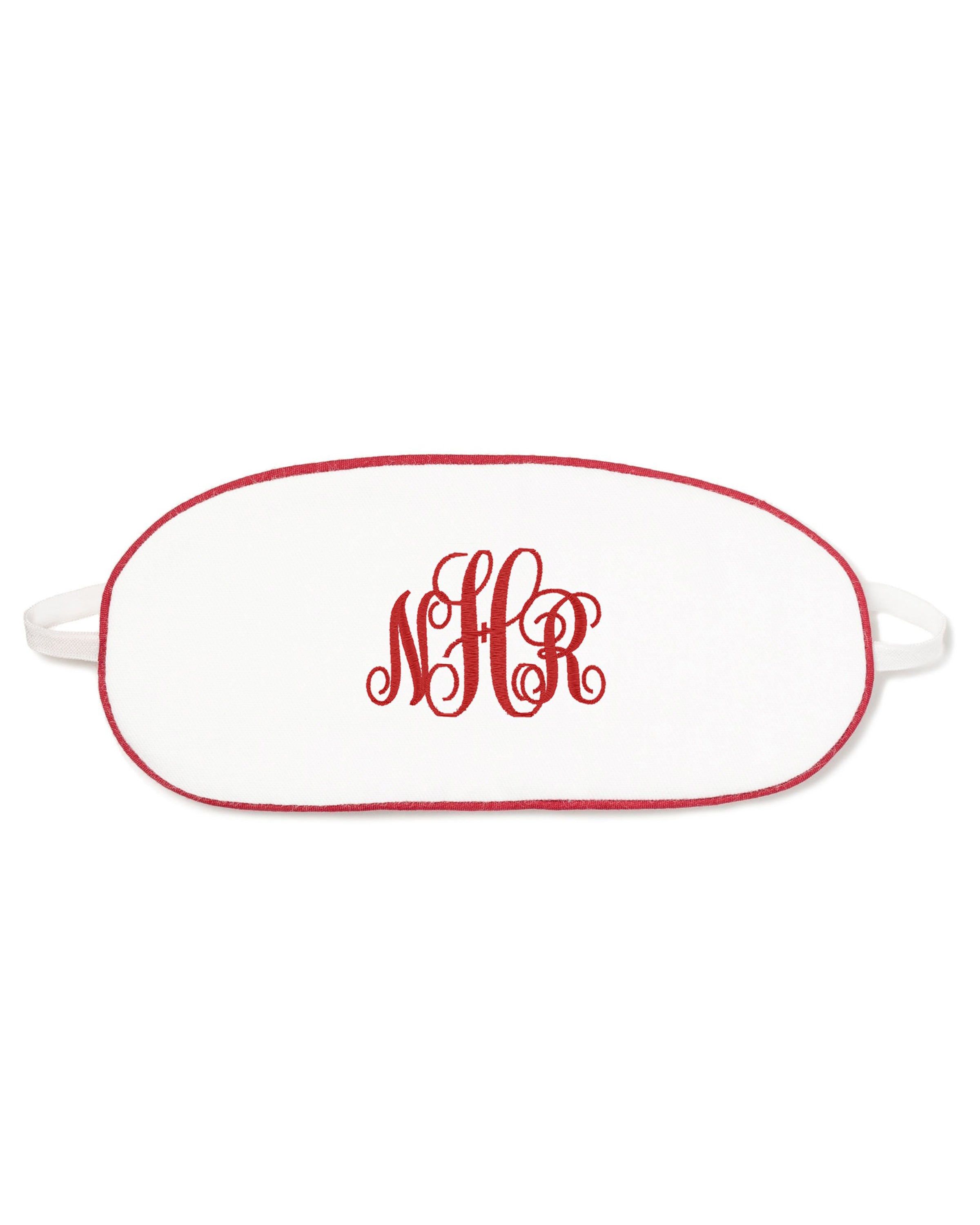 The Kids Twill Sleep Mask in White with Red Piping by Petite Plume is a luxurious sleepwear accessory featuring red embroidered NHR initials, elegant red piping, and elastic straps for a perfect fit.