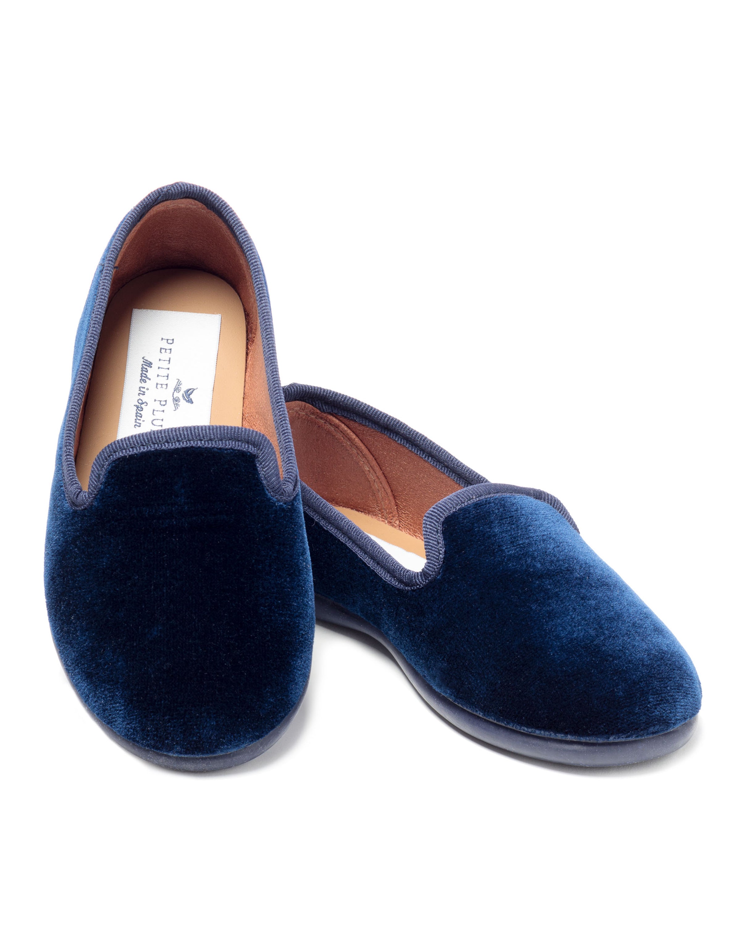 The Womens Hamptons Loafer in Navy Velvet by Petite Plume is crafted from luxe velvet with a subtle shine, featuring a soft pinkish-tan inner lining. One shoe faces forward slightly angled, while the other is tilted to reveal the insole and brand label.