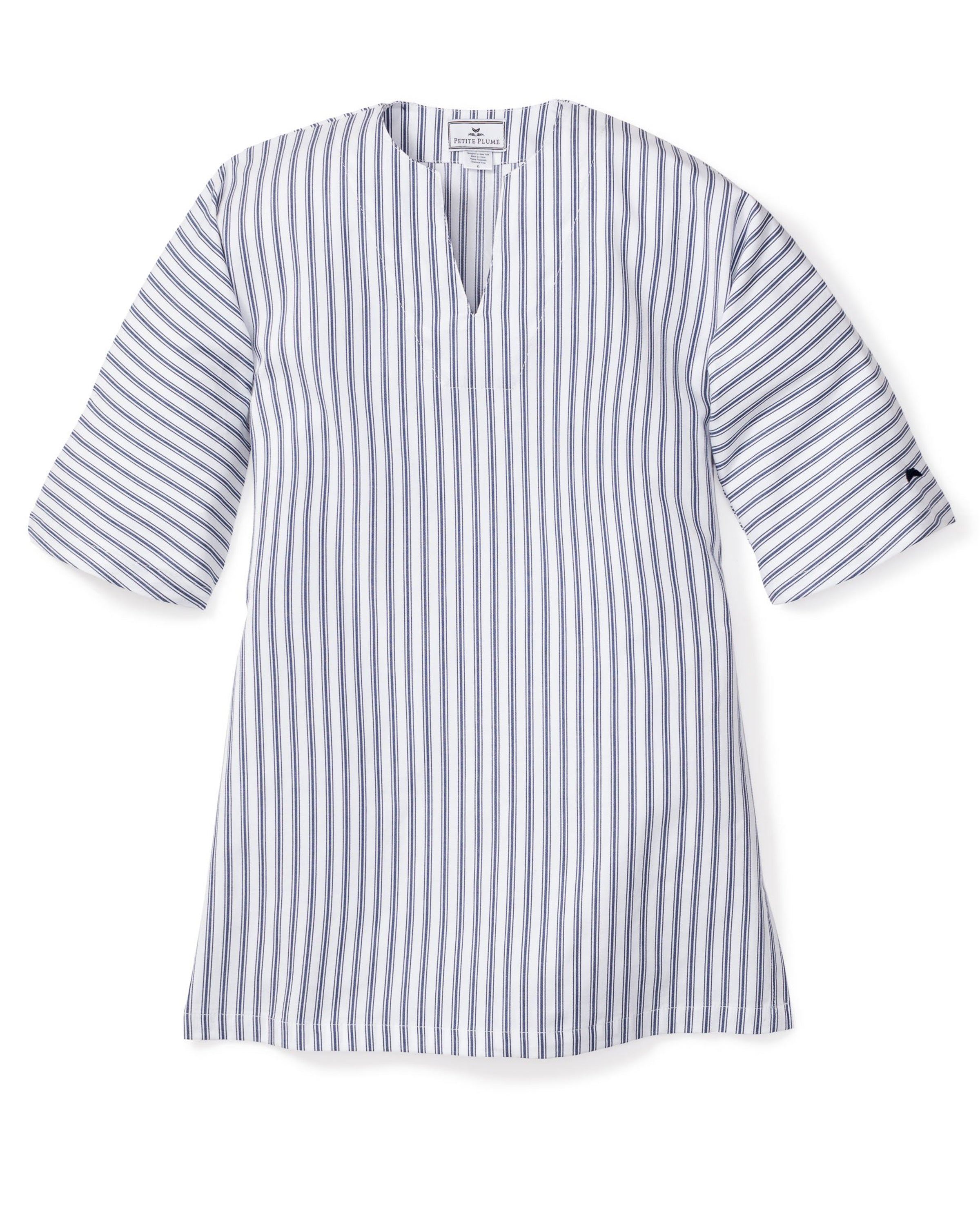 The Girls Twill Caftan in Navy French Ticking by Petite Plume is a blue and white vertical striped dress crafted from breathable cotton. It features elbow-length sleeves, a V-neckline, and a mid-thigh hemline, offering a tunic-like appearance reminiscent of luxurious sleepwear.