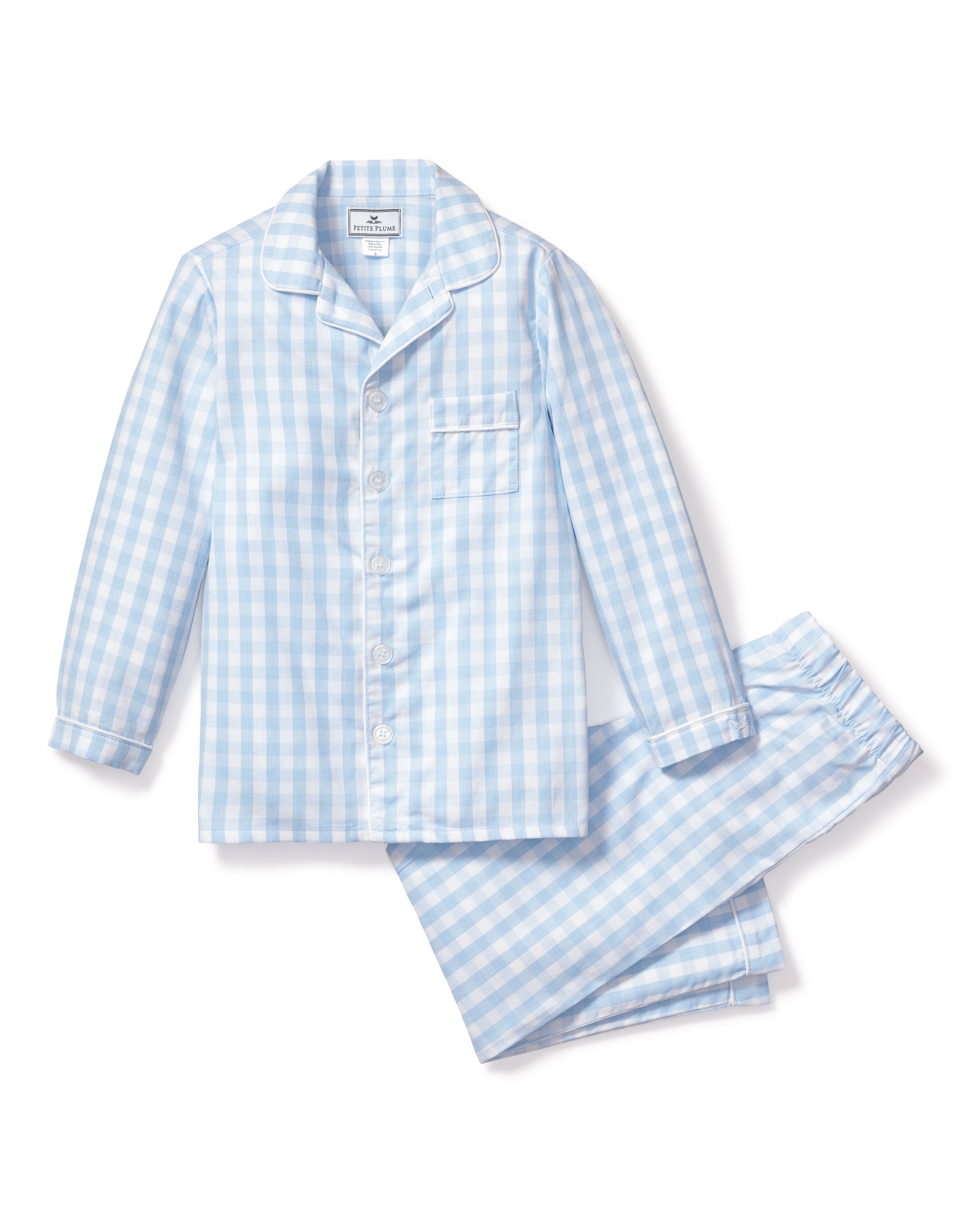 The Petite Plume Kids Twill Pajama Set in Light Blue Gingham includes a flame-retardant fabric with a classic checkered design. It features a long-sleeved button-up top with collar and chest pocket, plus matching pants, making it perfect for childrens sleepwear.