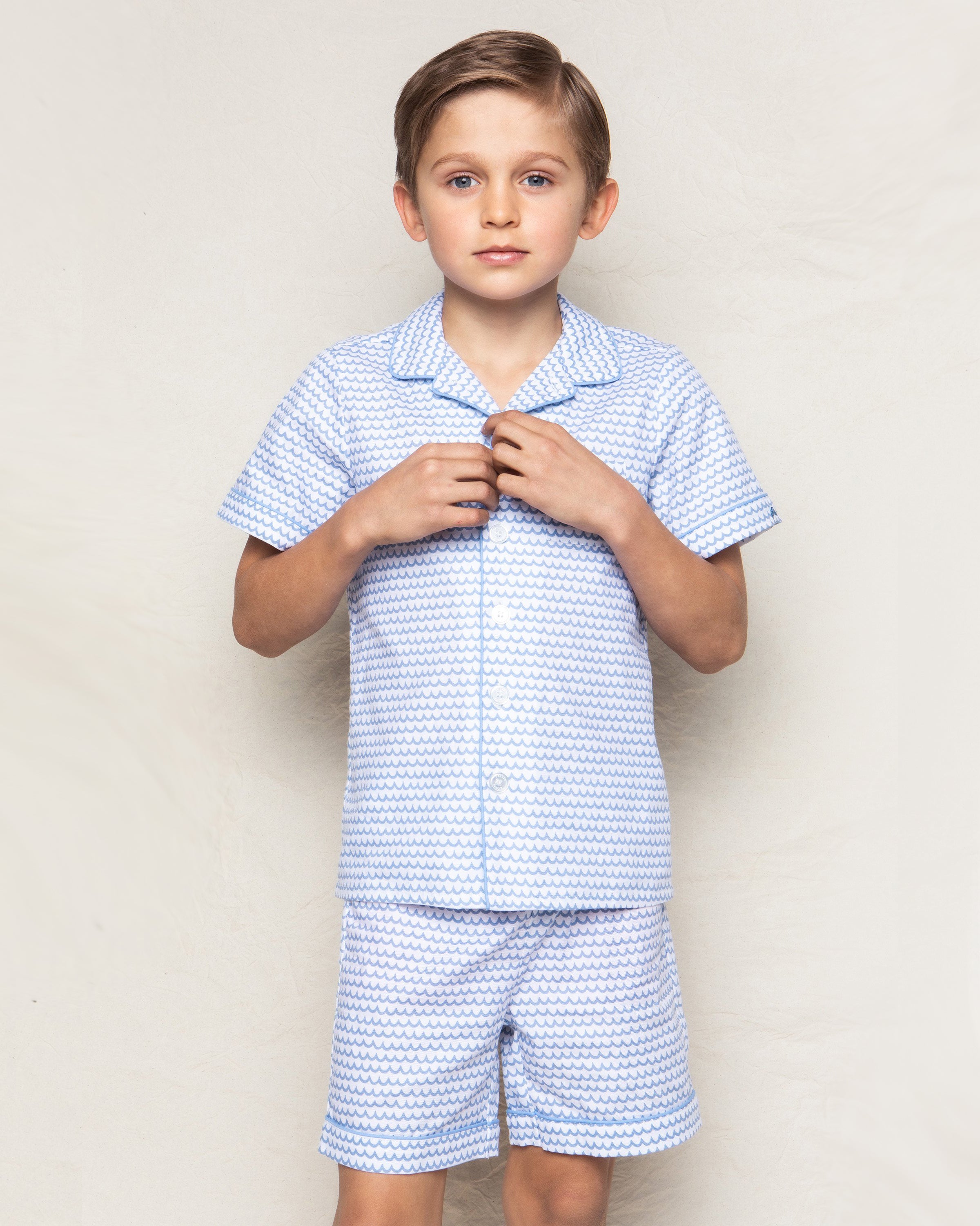 A young boy models Petite Plumes Kids Twill Pajama Short Set in La Mer, made from high-quality cotton, against a plain background, looking directly at the camera with a neutral expression.