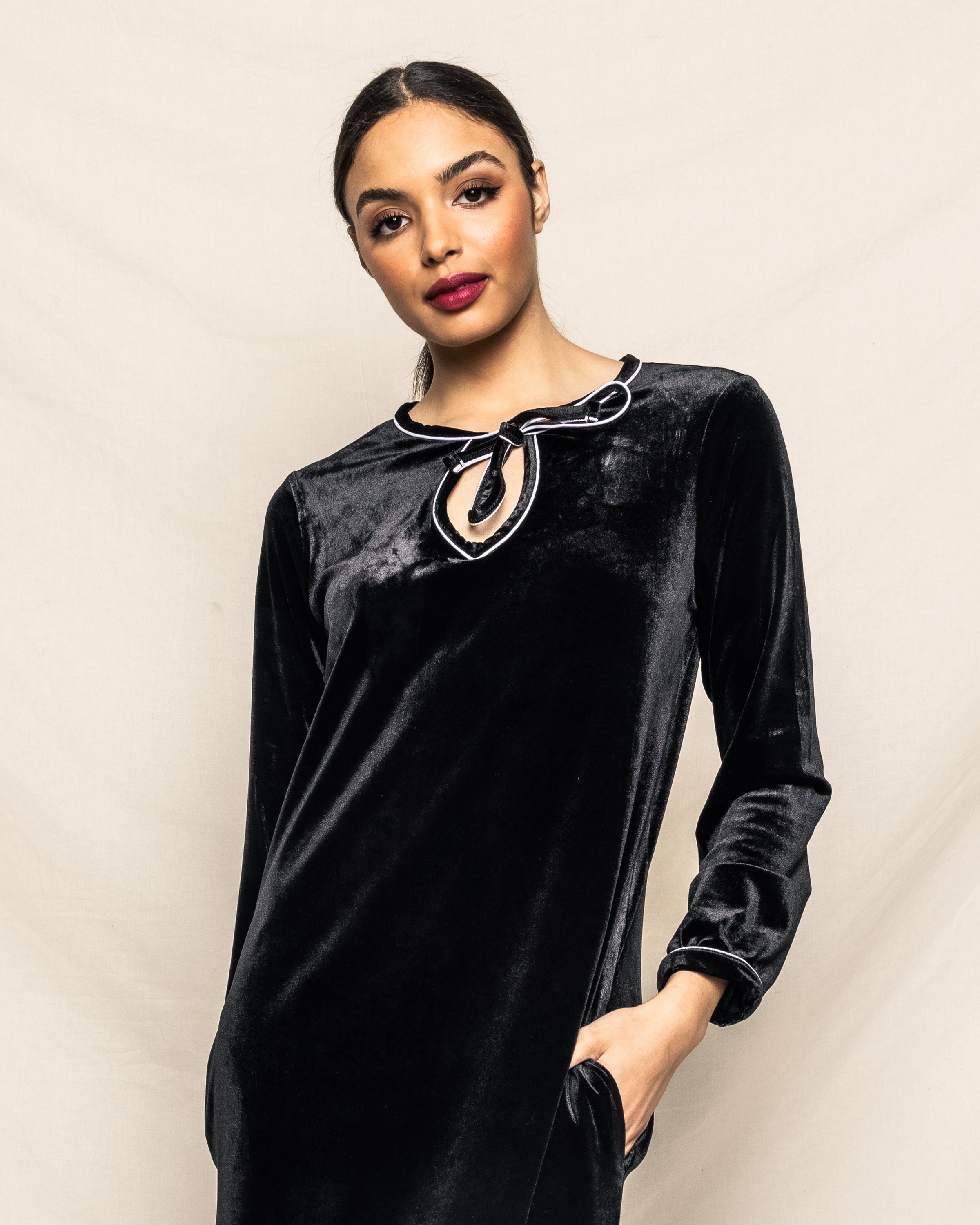 Dressed in a Petite Plume Womens Velour Harlow Nightgown in Black, adorned with a loop detail at the neckline, they pose with their long hair pulled back against a neutral backdrop, exuding classic Hollywood style.