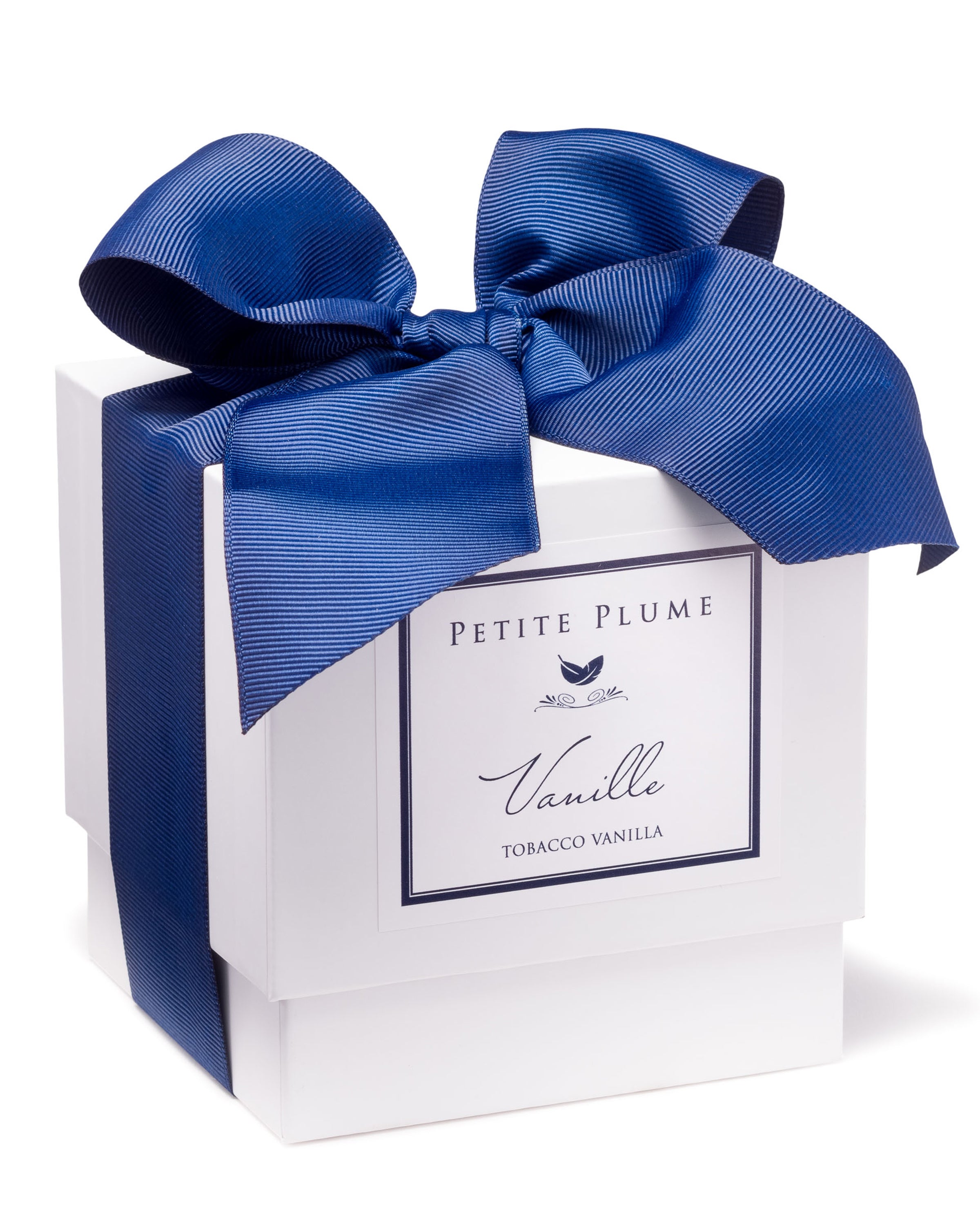 A white gift box with a large, elegant blue bow and a Petite Plume label hints at the richness of the Luxe Vanille Candle inside, promising an exquisite, luxurious aroma.