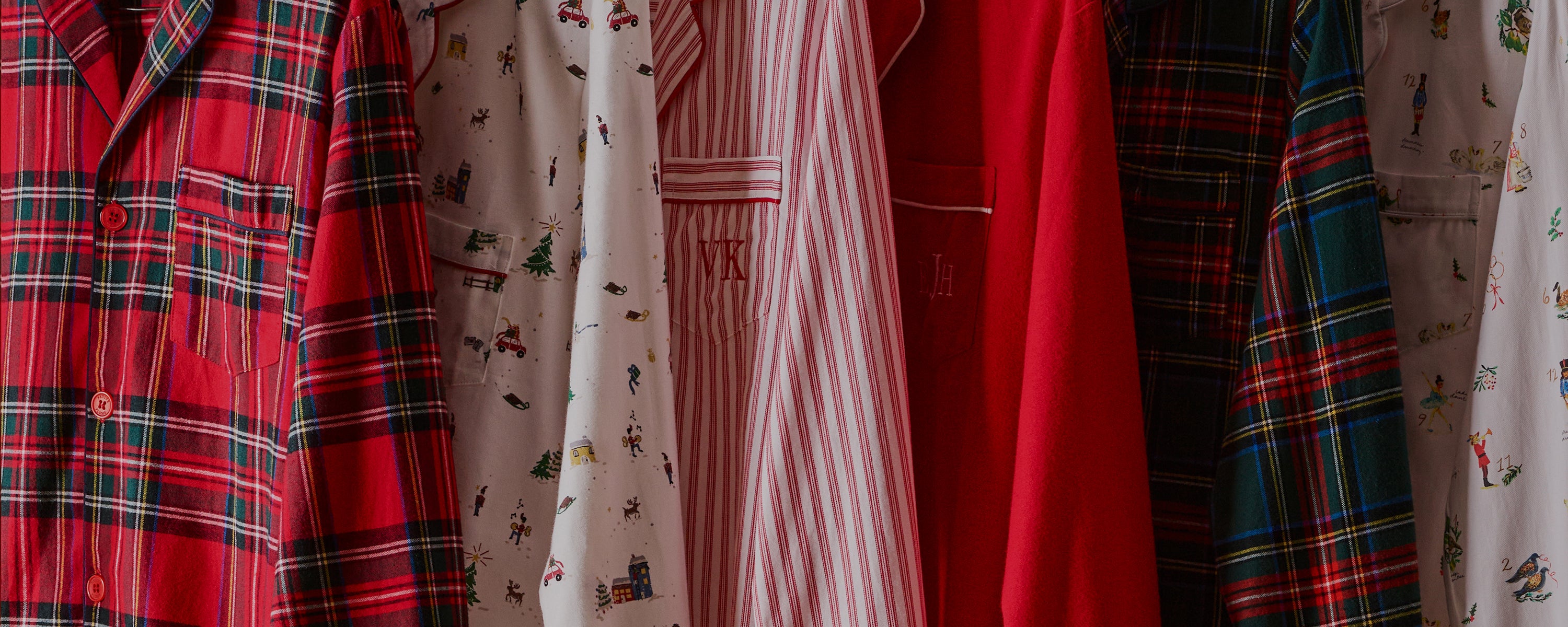 Several button-up pajama tops hang side by side, featuring various patterns including red plaid, holiday-themed prints, red and white stripes, solid red, and green plaid.