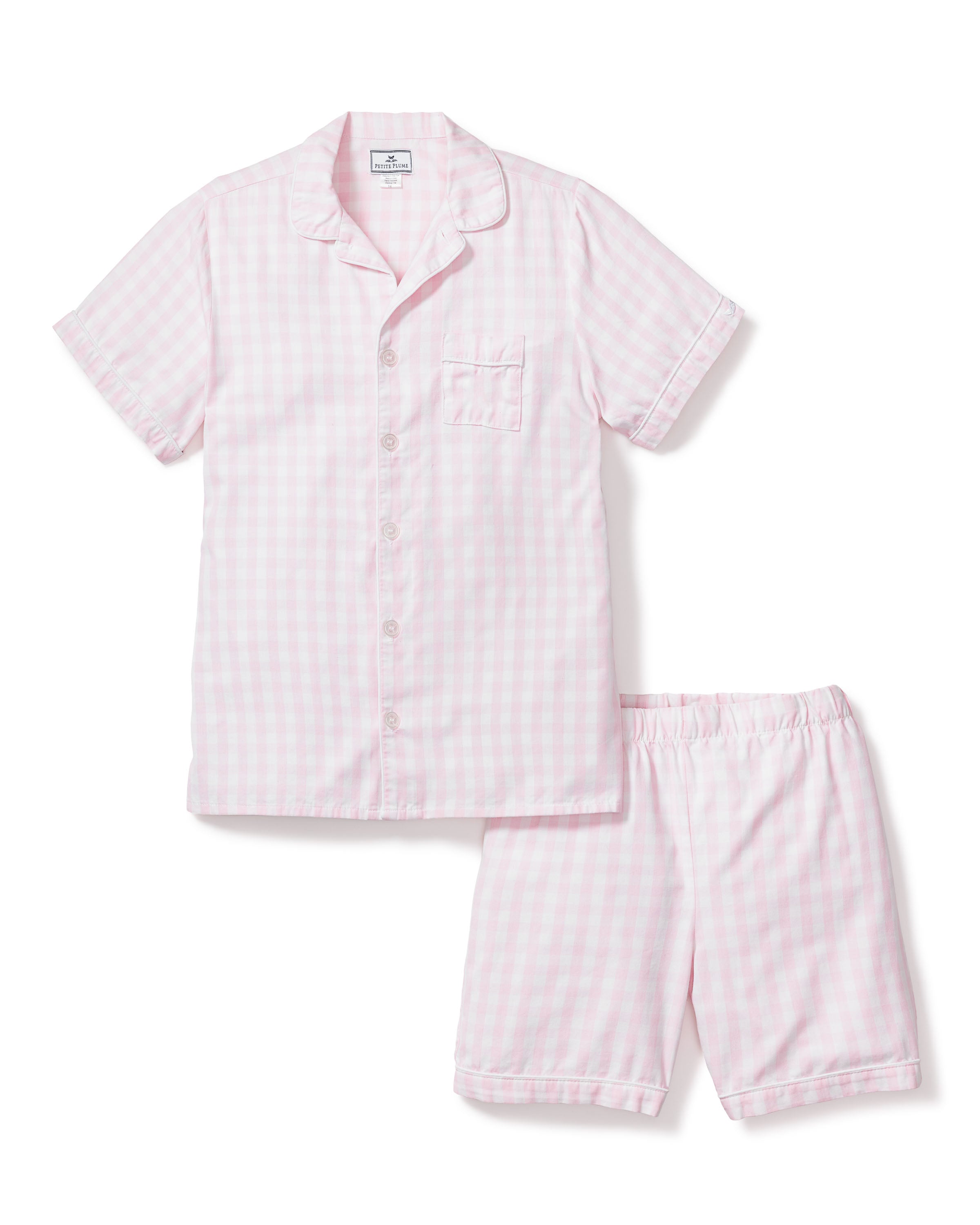 The Kids Twill Pajama Short Set in Pink Gingham by Petite Plume is a luxurious sleepwear choice, featuring a gingham print with a pink and white checkered short-sleeve button-up shirt that has a chest pocket, paired with matching elastic waist shorts made from soft yarn-dyed cotton.