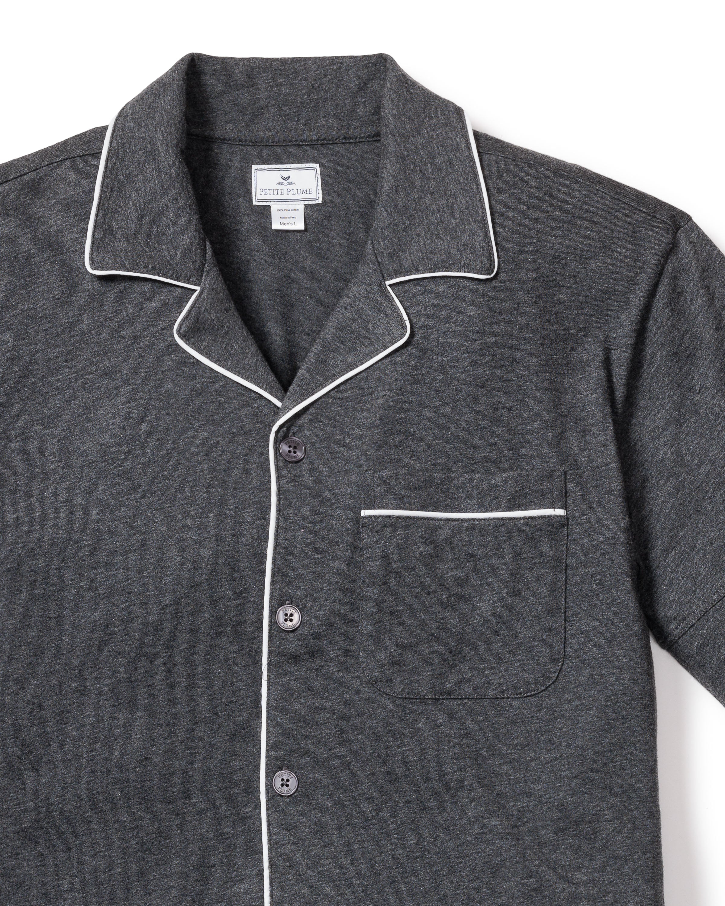 The Mens Pima Pajama Short Set by Petite Plume in Dark Heather Grey features a dark gray shirt with white piping on the collar, cuffs, and pocket outline. It includes a chest pocket and three buttons, made from soft yarn-dyed fabric, likely a cotton or Peruvian Pima cotton blend for a textured feel.