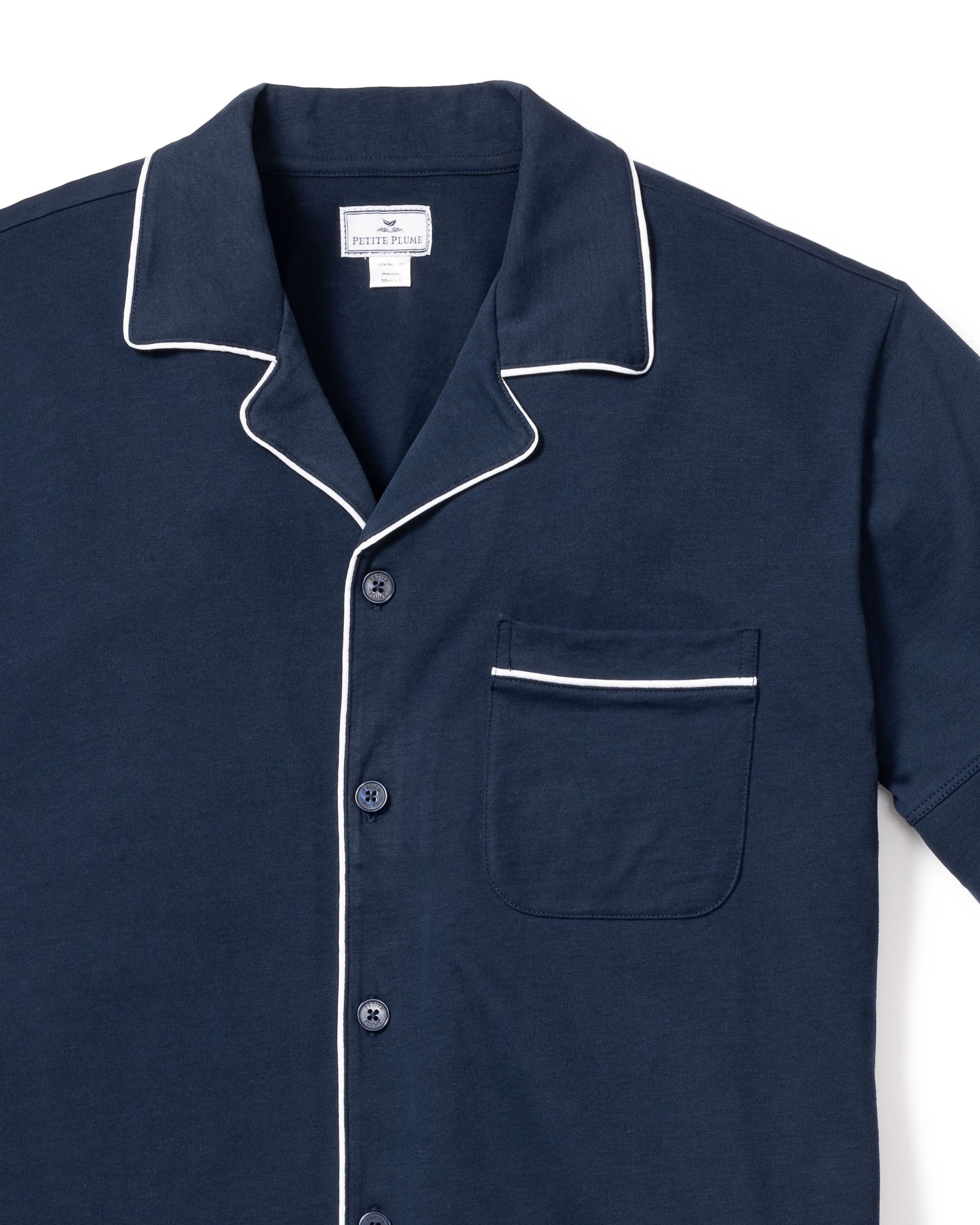 The Mens Pima Pajama Short Set in Navy by Petite Plume features a luxurious Peruvian Pima cotton button-up shirt with white piping on the collar, cuffs, and pocket. Its jersey knit design includes a chest pocket and neck label for comfort and elegance during sleep.