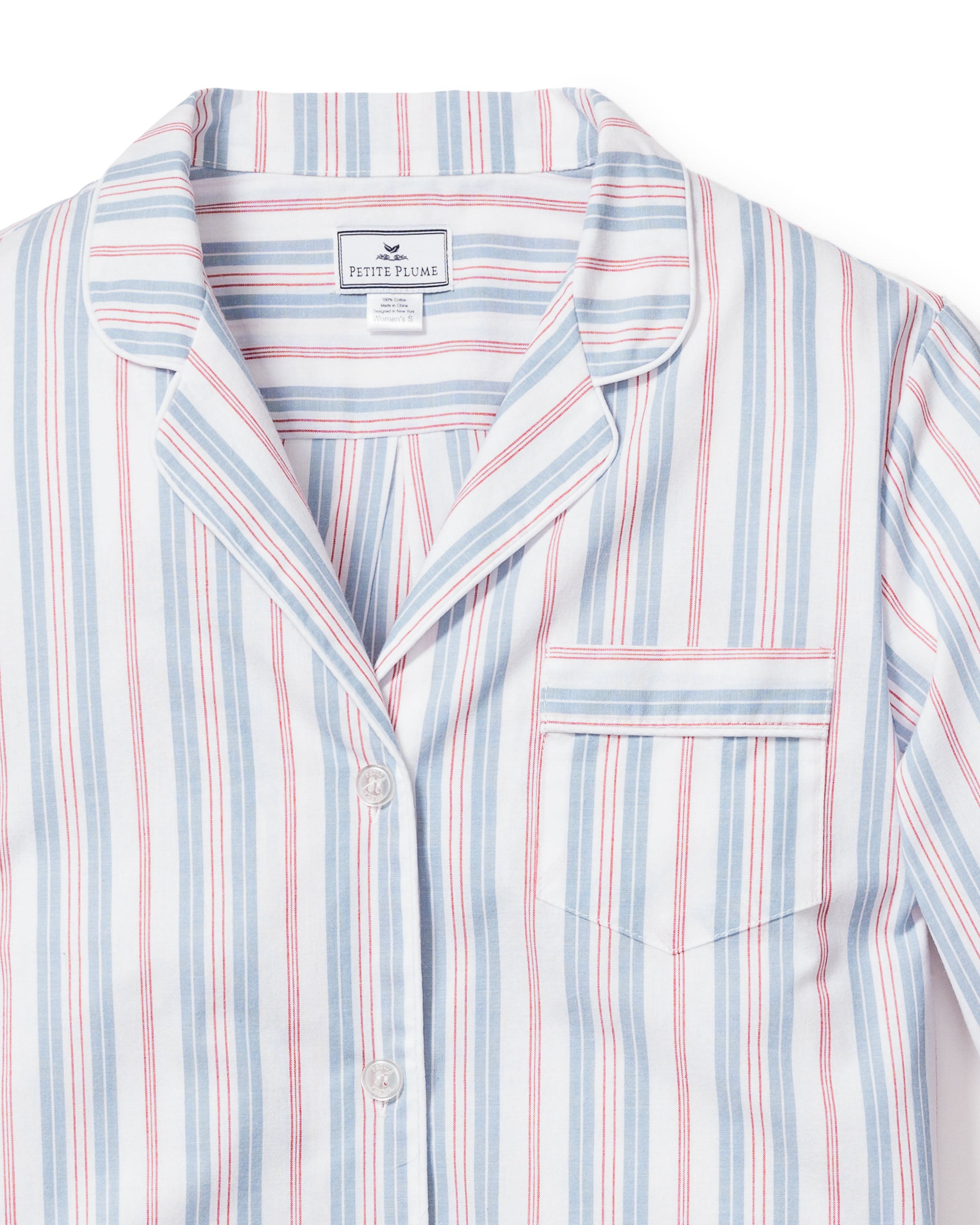 A close-up of the Womens Twill Pajama Set in Vintage French Stripes reveals a collared, button-top with luxurious cotton featuring blue, pink, and white vertical stripes. The chest pocket complements the Petite Plume label inside, adding elegance.