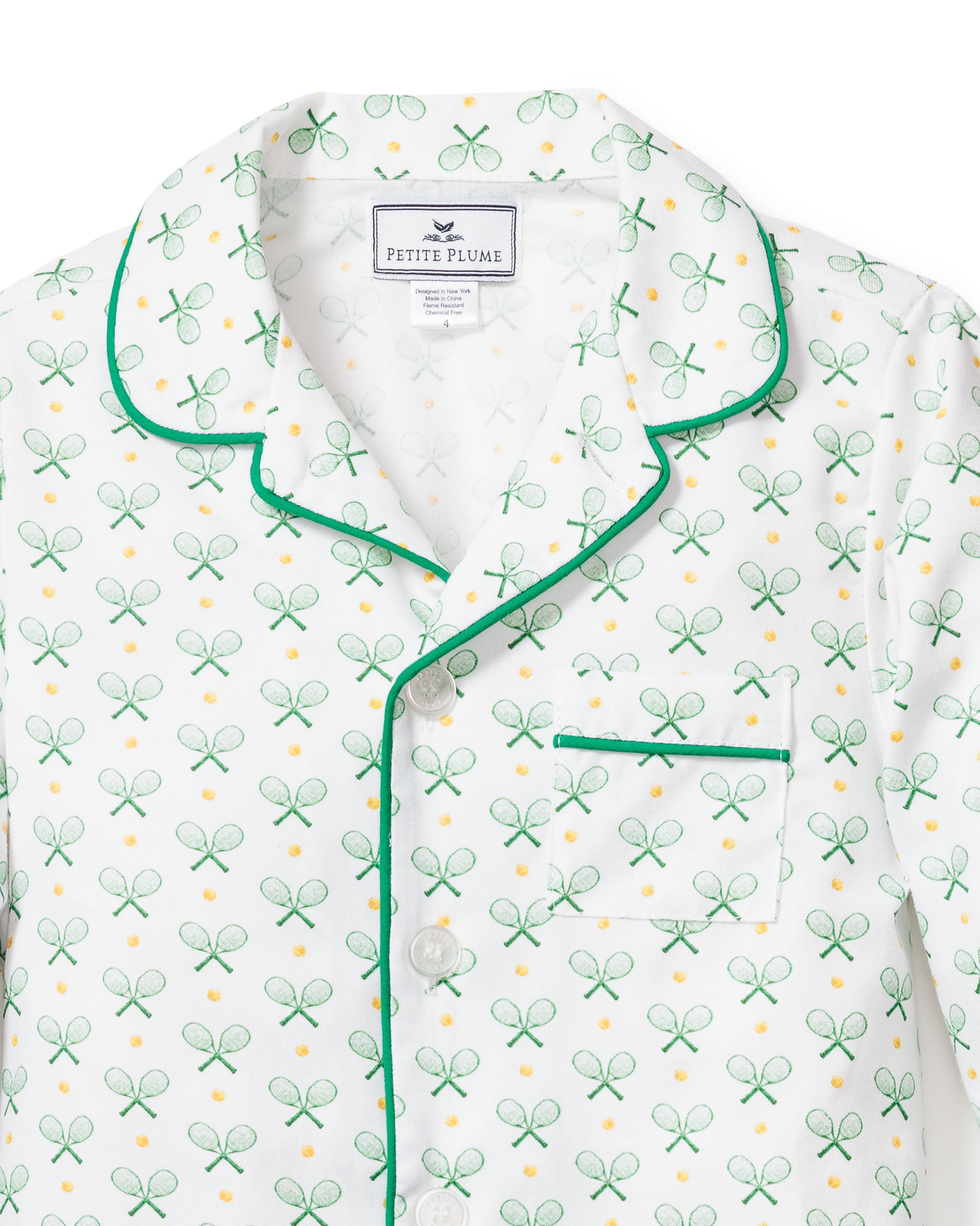 The Kids Twill Pajama Short Set in Match Point by Petite Plume includes a luxurious white top with a green tennis racket and ball pattern, complemented by subtle green piping on the collar, front, and pockets.