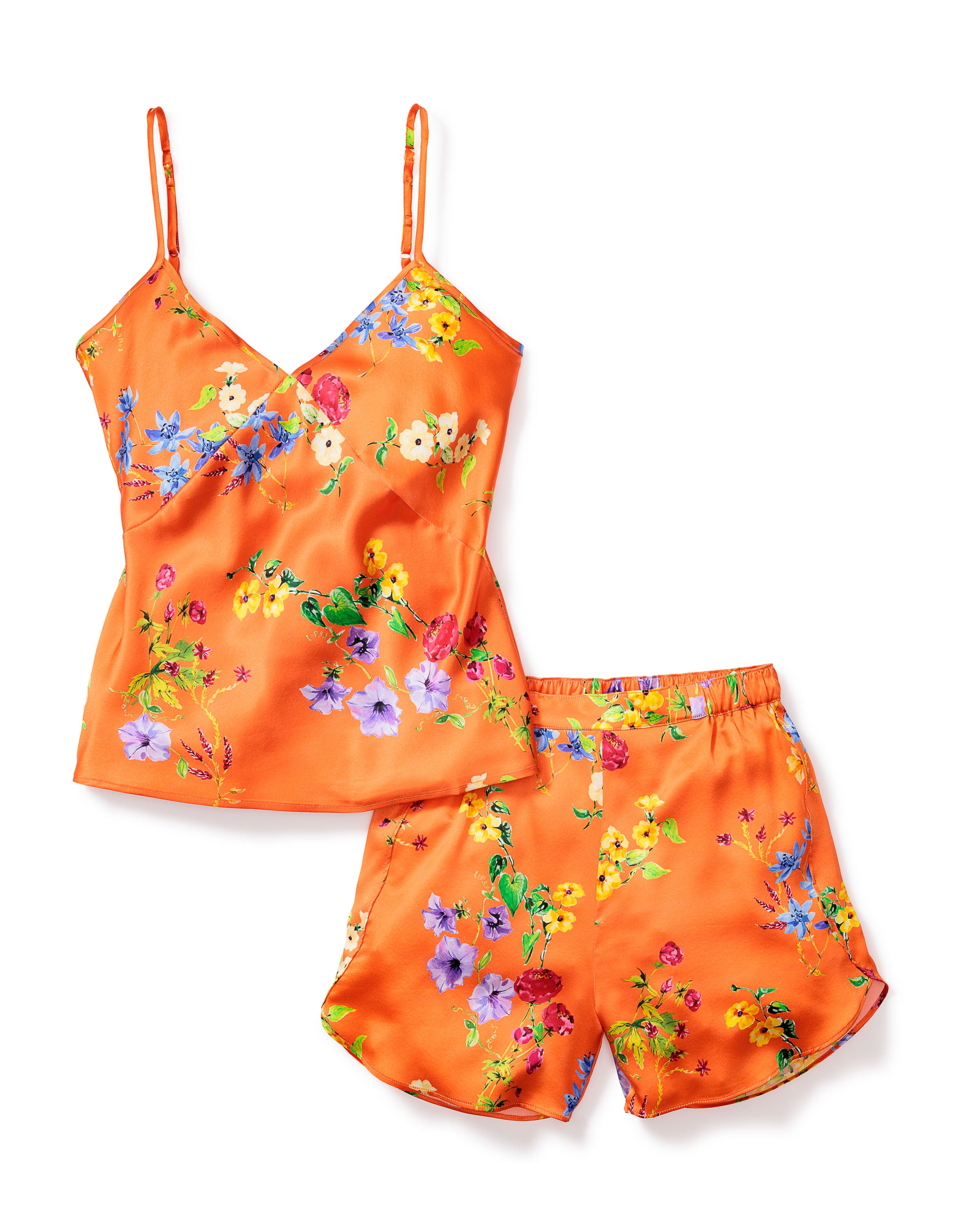 The Womens Silk Cami Short Set in Tangerine Brilliant Botanical by Petite Plume features a luxurious satin camisole with thin straps and matching shorts, both showcasing a vibrant botanical print in shades of yellow, blue, and purple.
