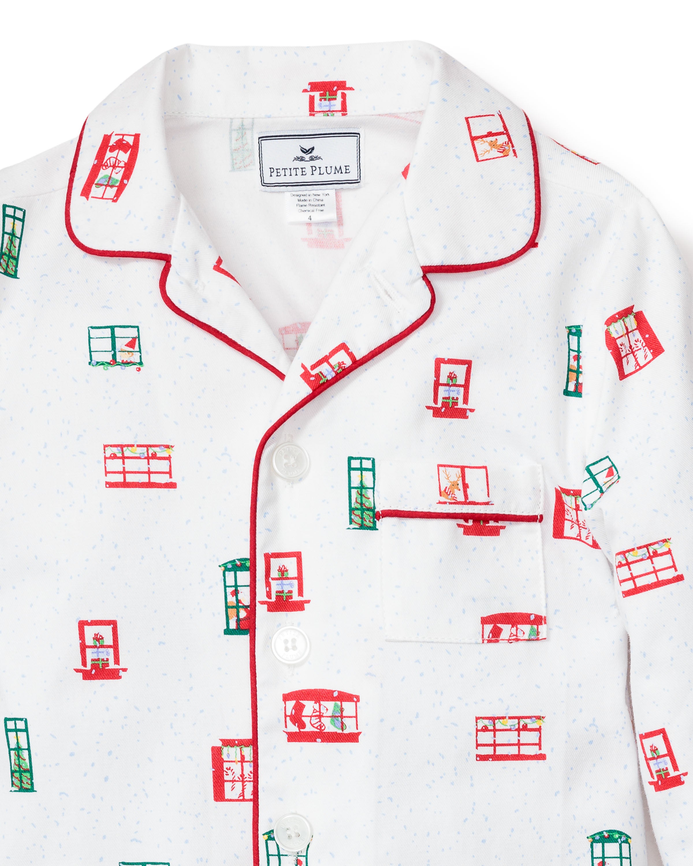 The Petite Plume Kids Maisonette x Petite Plume Night Before Pajama Set features white pajamas with red piping and a festive green and red window print, complete with a chest pocket. Perfect for those who enjoy luxurious sleepwear.