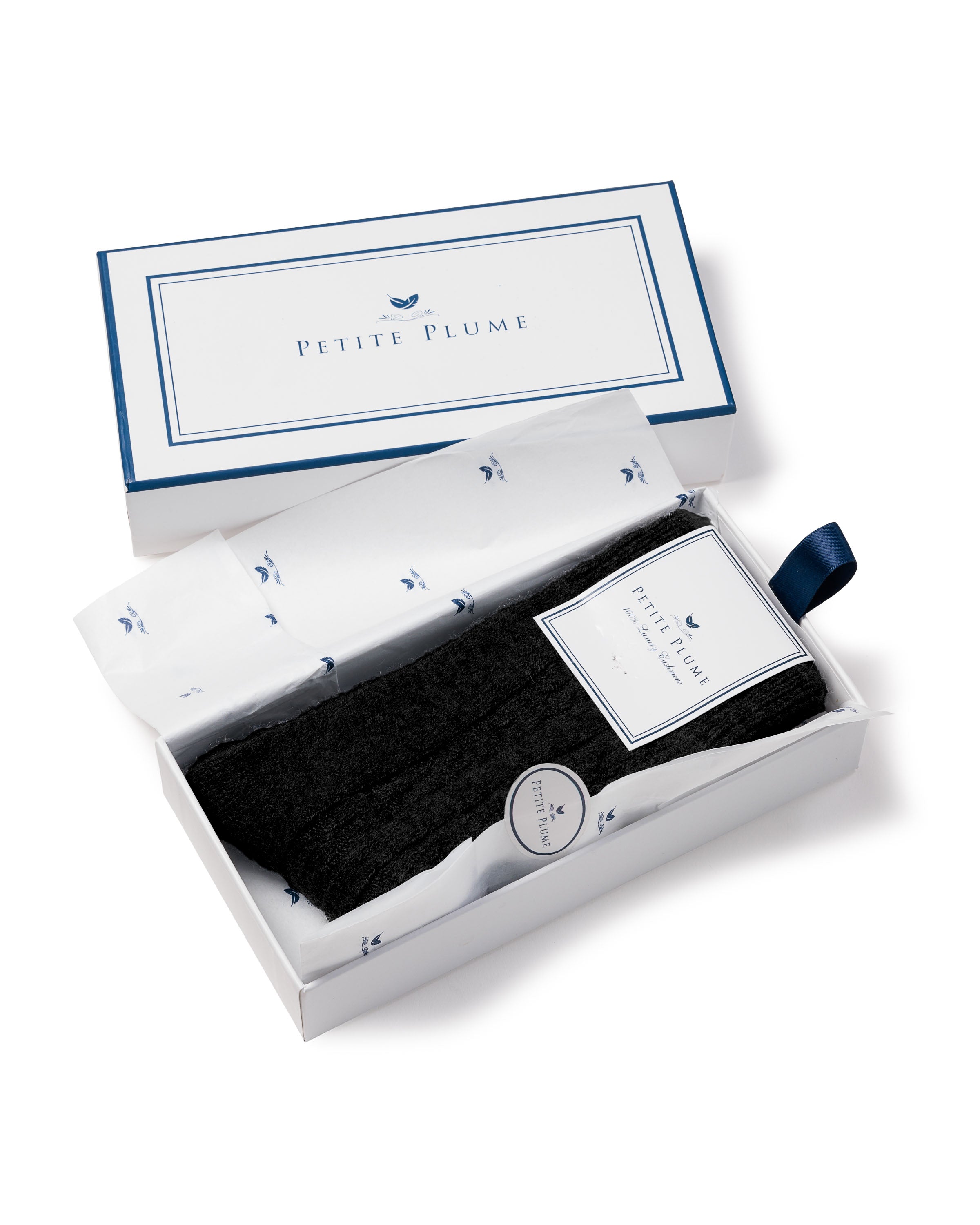 The black cashmere socks by Petite Plume offer plush texture and luxurious comfort, elegantly packaged in a white box with tissue paper featuring blue bird motifs and a blue ribbon pull tab.