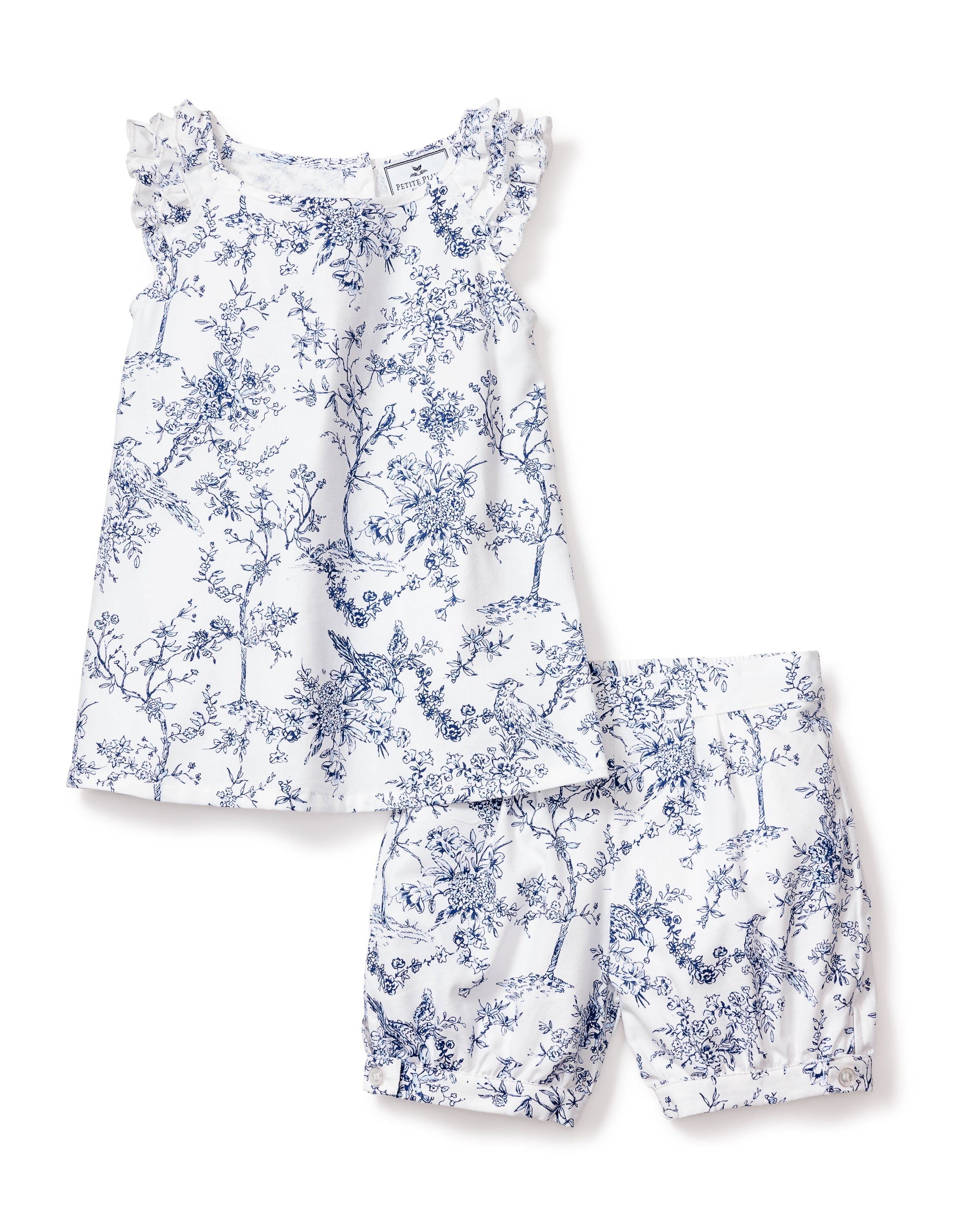The Petite Plume Girls Twill Amelie Short Set in Timeless Toile features a white sleeveless top with ruffled sleeves and shorts with an elastic waistband and ruffled hems, adorned with blue floral and bird patterns, offering a luxury botanical sleepwear vibe.