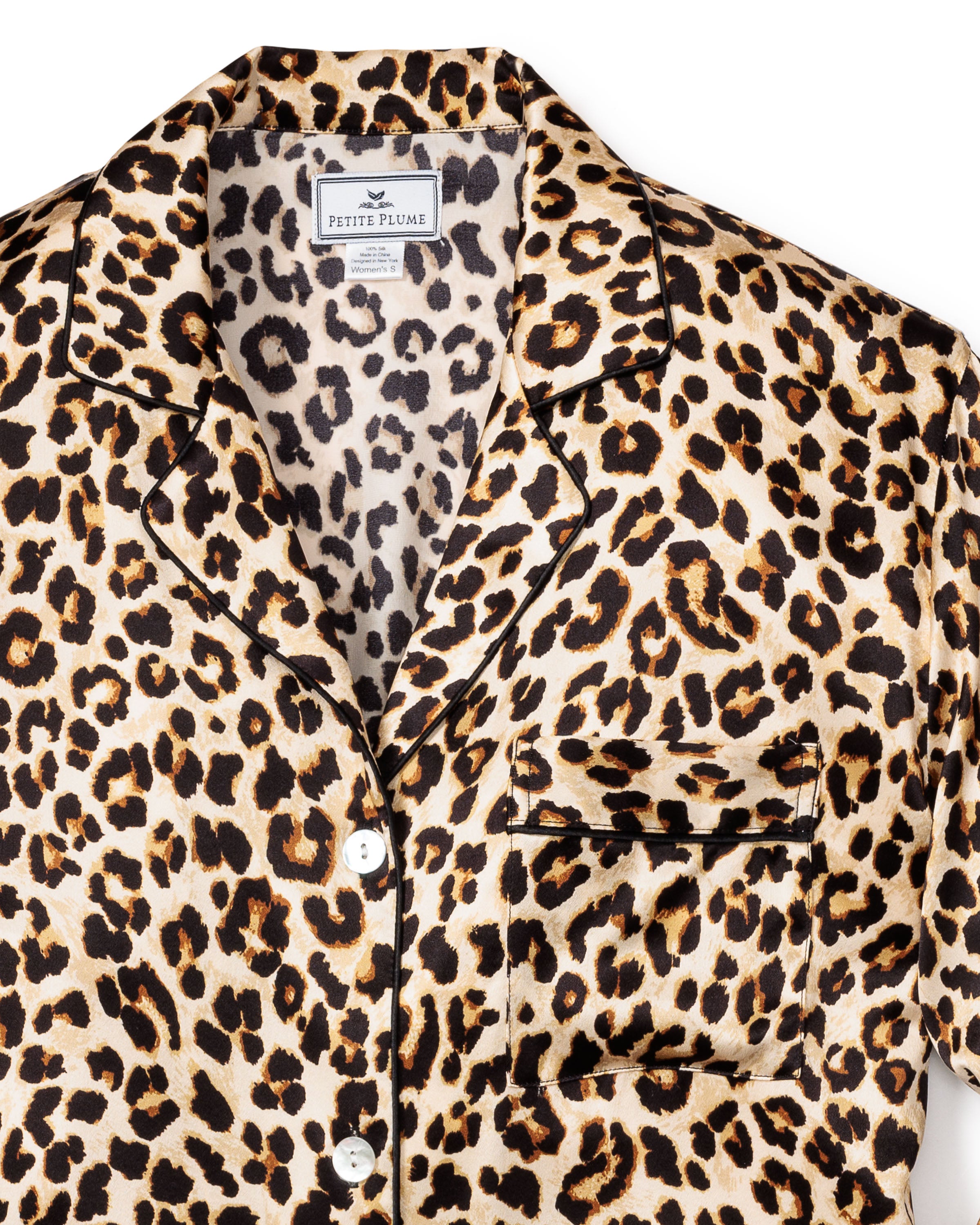 The Veronica Beard x Petite Plume Womens Silk Nightshirt in Leopard showcases a luxurious leopard print crafted from 100% Mulberry silk. It features black piping, a notched collar, white buttons, and a small chest pocket, all enhanced by the fabrics glossy finish.