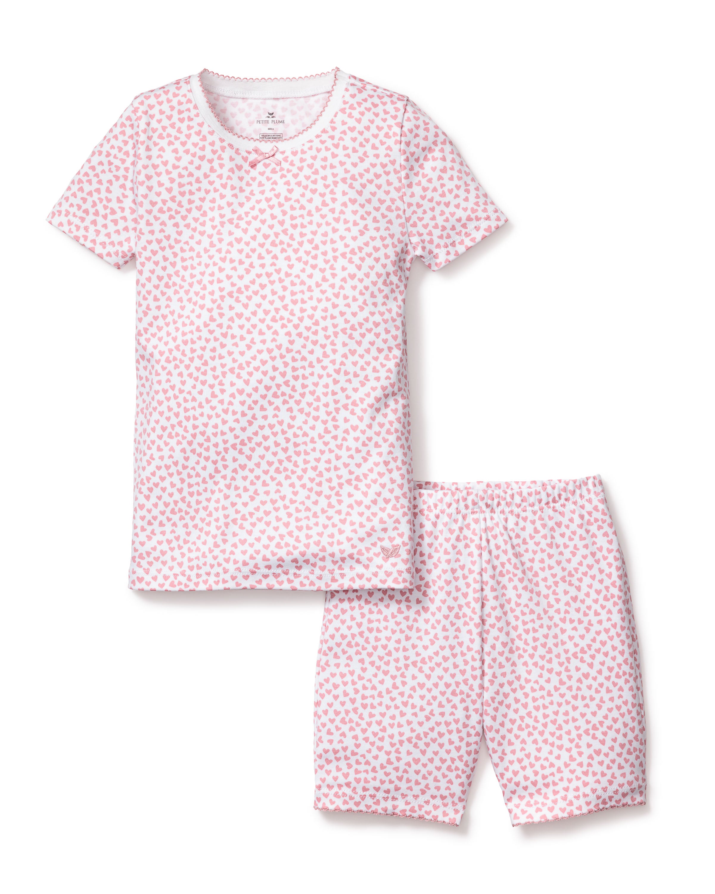 The Kids Pima Snug Fit Pajama Short Set in Sweethearts by Petite Plume is a luxury childrens sleepwear set featuring short-sleeved white pajamas with pink heart patterns. Made from pima cotton, it includes a round-neck top and scalloped-edged shorts for added charm.