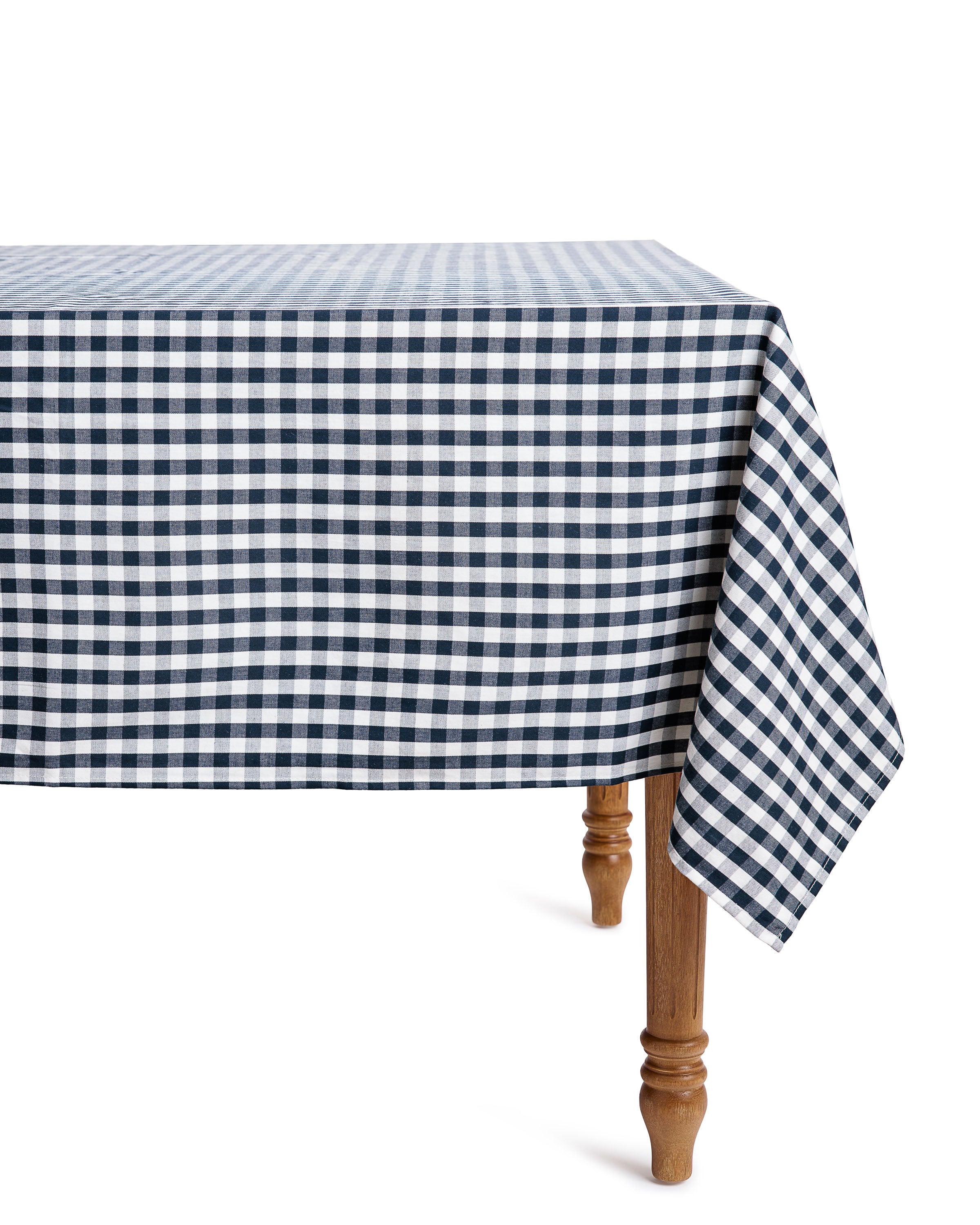 A Signature Twill Tablecloth in Navy Gingham by Petite Plume, made of 100% cotton, elegantly drapes over a table. Its checkered design and the wooden turned legs create a charming, casual yet neat appearance, perfect for a festive tablescape.