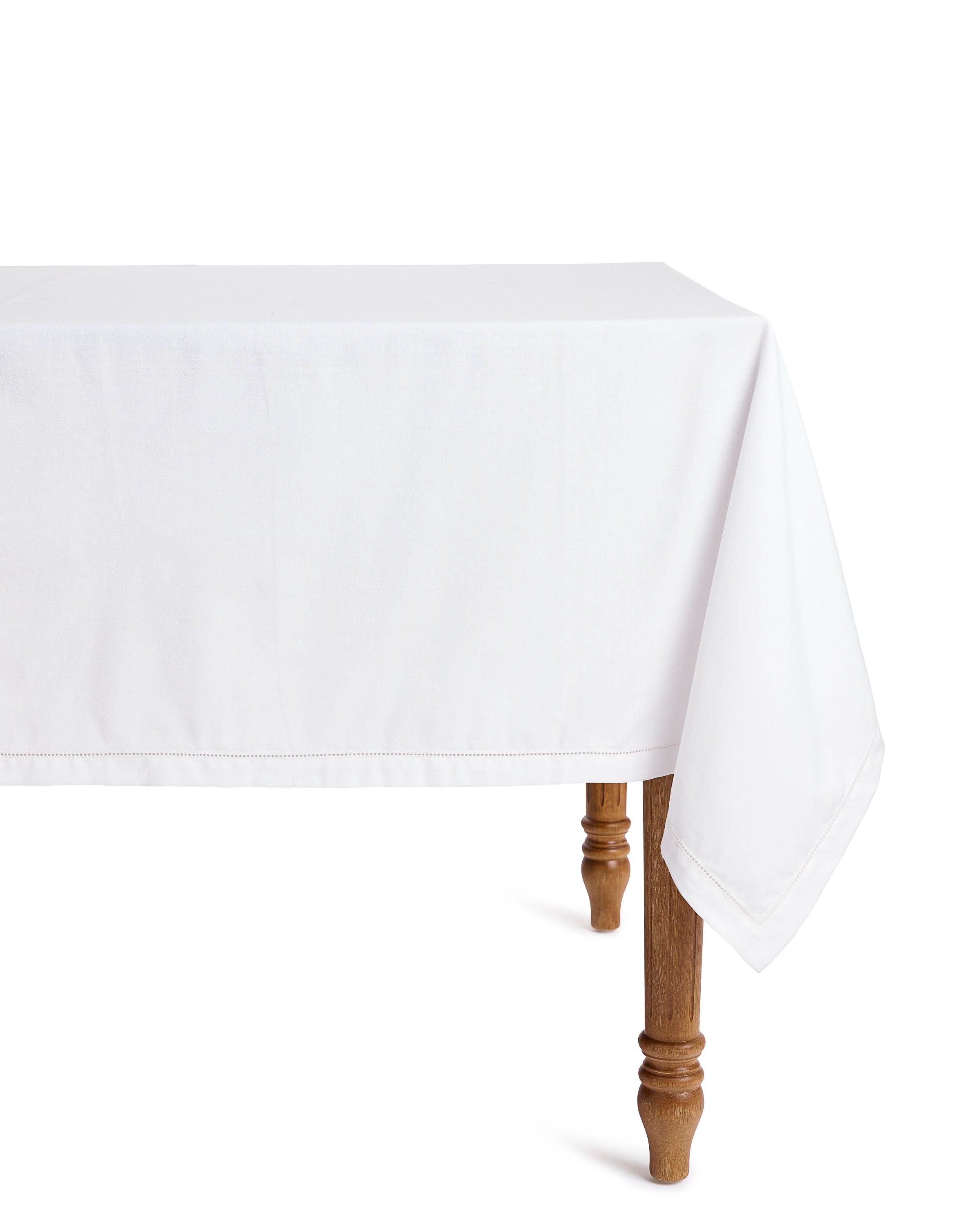 A wooden table with intricately carved legs is adorned with a Signature Twill Tablecloth in White by Petite Plume, draped evenly over the side.