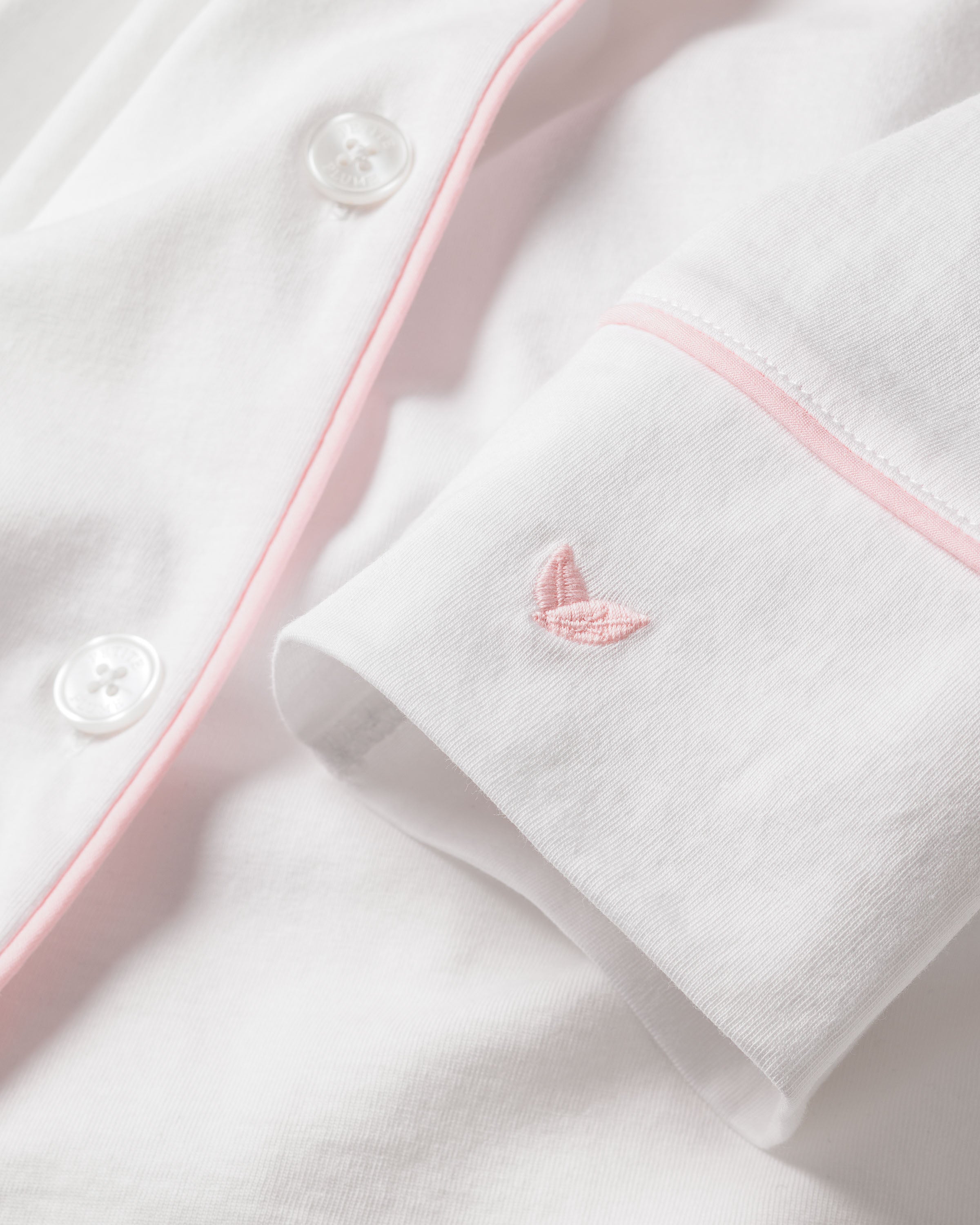 The Womens Pima Pajama Set by Petite Plume features luxurious Peruvian Pima cotton in white with pink piping, a delicate pink embroidered logo on the sleeve cuff, and white buttons. This set epitomizes sophisticated comfort with its exceptionally soft and smooth fabric.