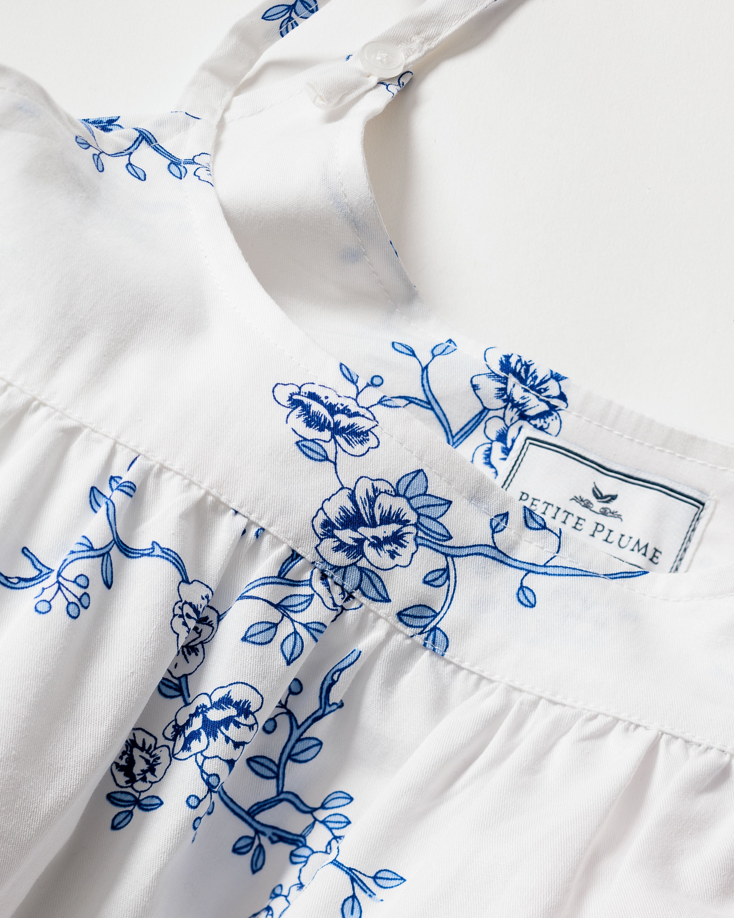 The Womens Twill Chloé Nightgown in Indigo Floral by Petite Plume features a white base with blue floral vintage print near the top, thin straps, and gathers below the chest. It showcases luxury sleepwear on a plain light background.