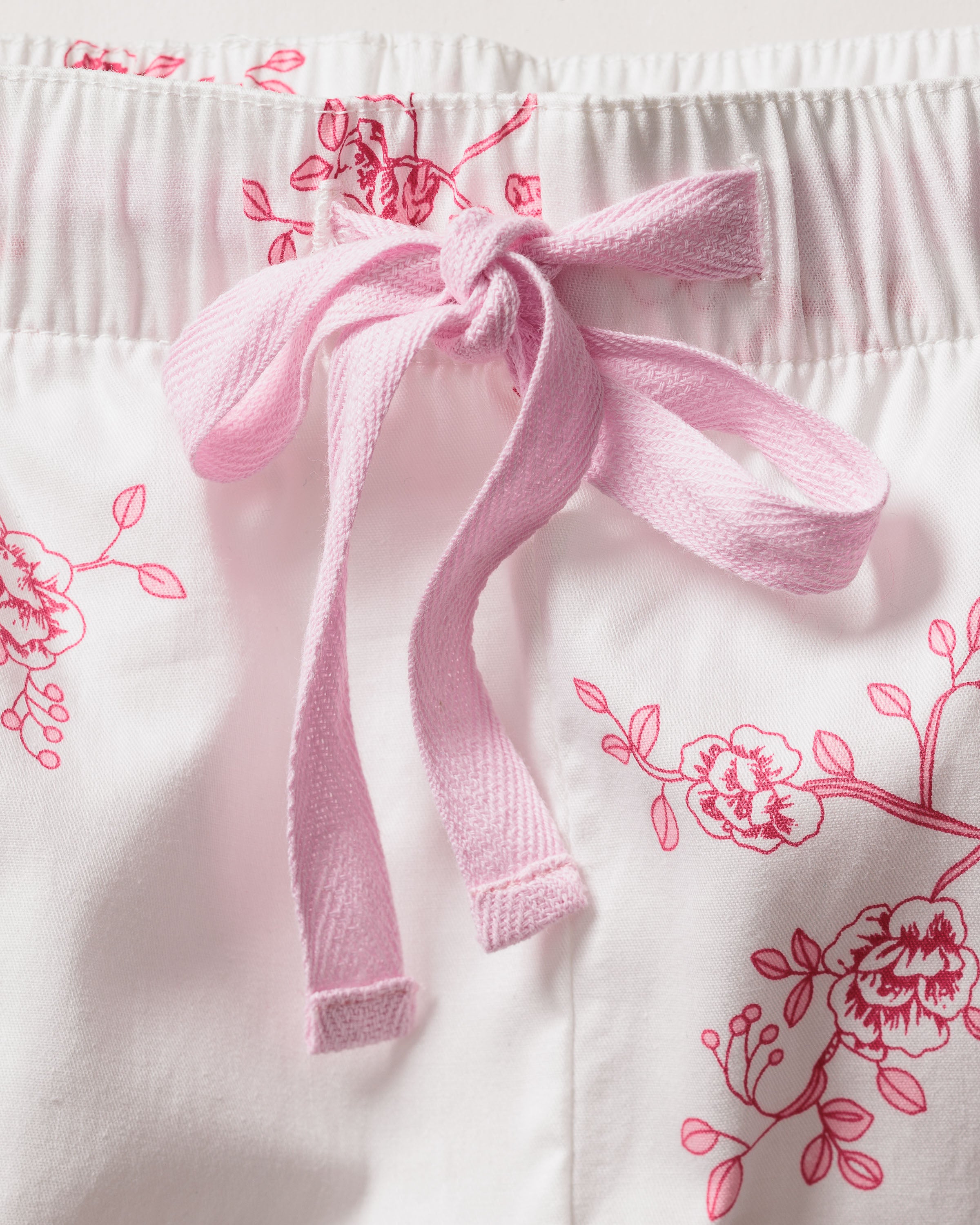 The Womens Twill Pajama Set in English Rose Floral by Petite Plume features premium cotton with white fabric adorned with pink florals and a bow-tied pink drawstring. Its elastic waistband ensures both style and comfort.