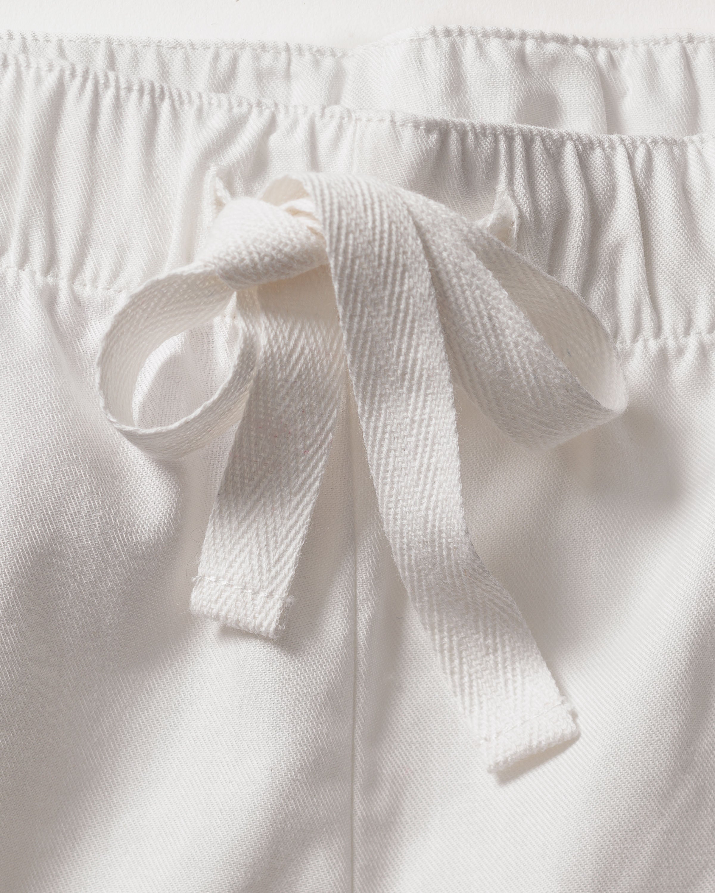 Close-up of Petite Plumes Womens Twill Pajama Short Set in White, featuring drawstring pants with an elastic waistband tied neatly. Crafted from high-quality cotton, the soft and textured fabric exemplifies luxurious sleepwear.
.
