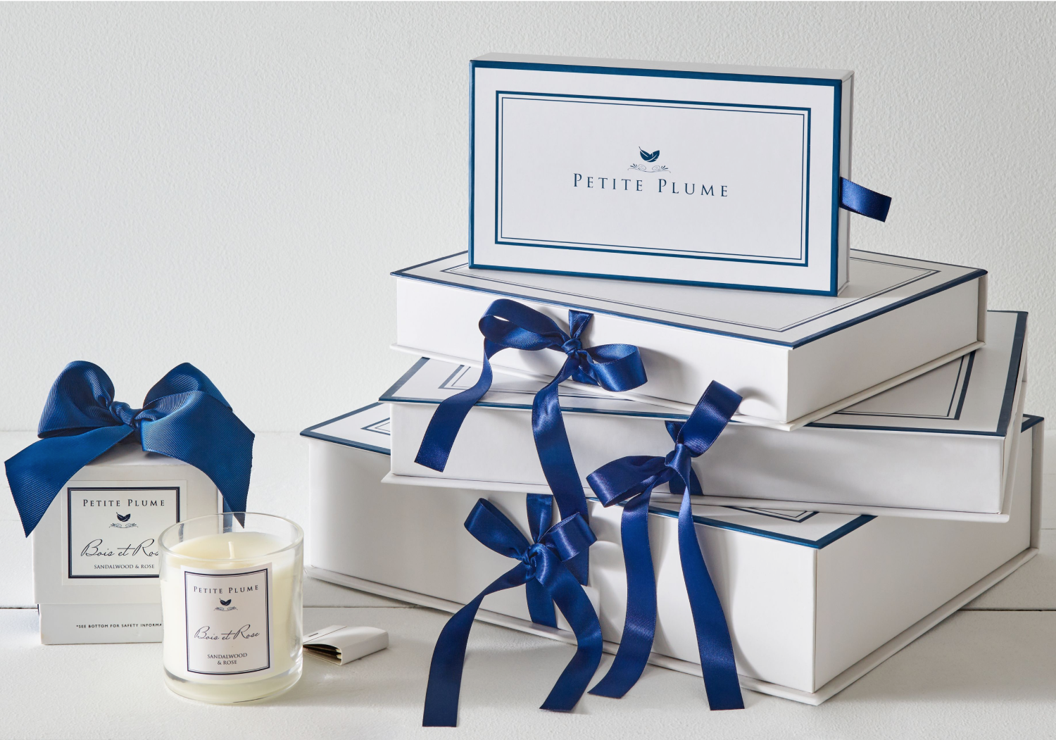 White and Navy gift boxes with navy boxed stacked on top of each other. To the left is a candle with matching gift box