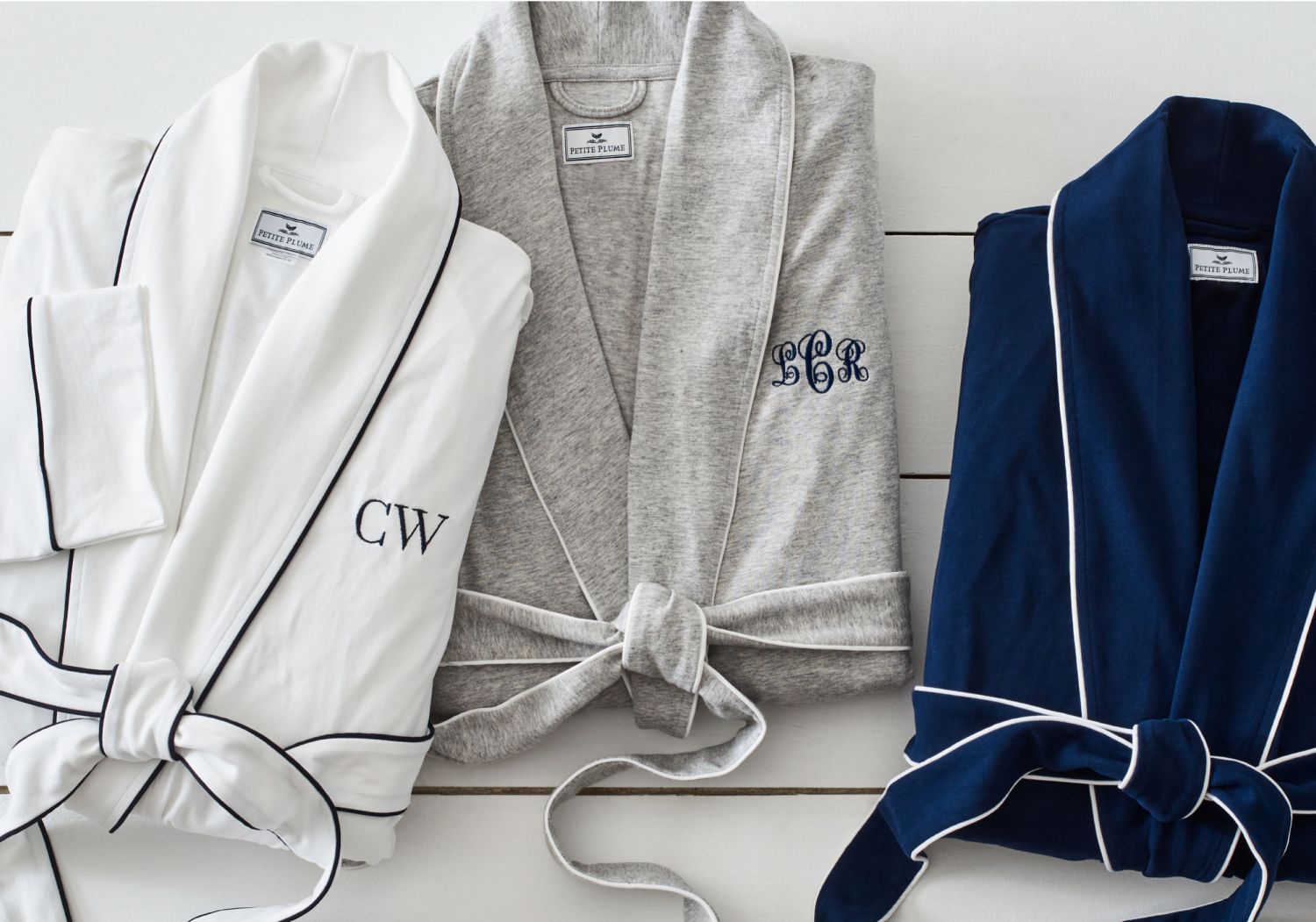 A white, grey and navy robe folded up with initials monogrammed on the right side of the robe