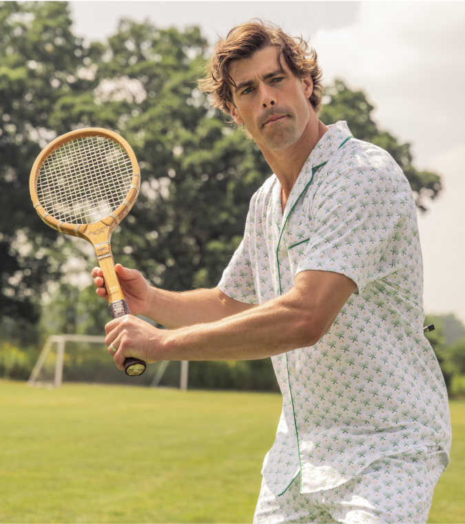 Man outside with a tennis racket wearing a pajama short set with green tennis rackets print