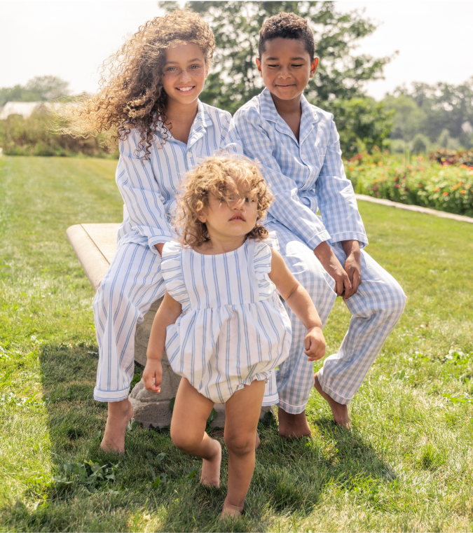 Three young children with curly hair in white and blue pajamas outside in a garden 