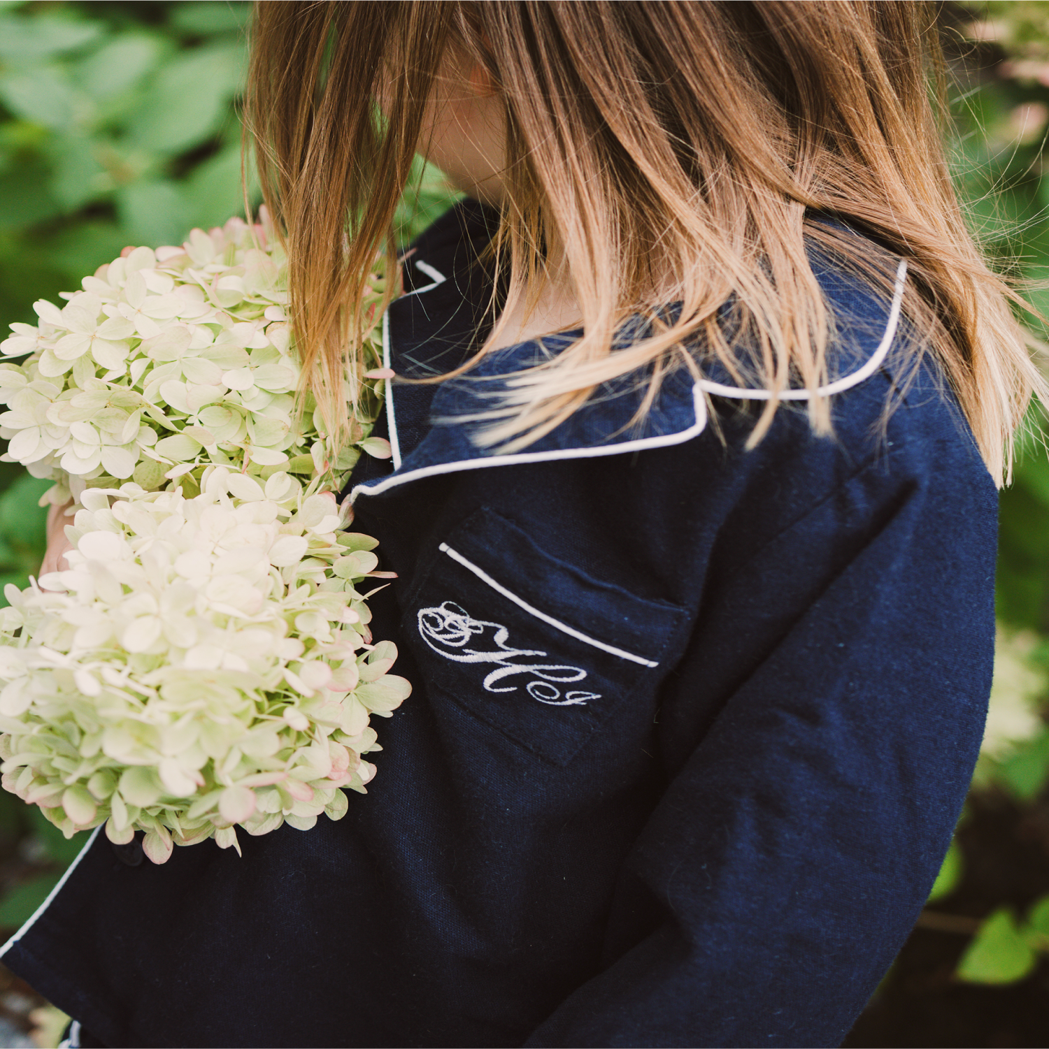 Close up of young girl with long light brown in Navy pajama set holding white flowers