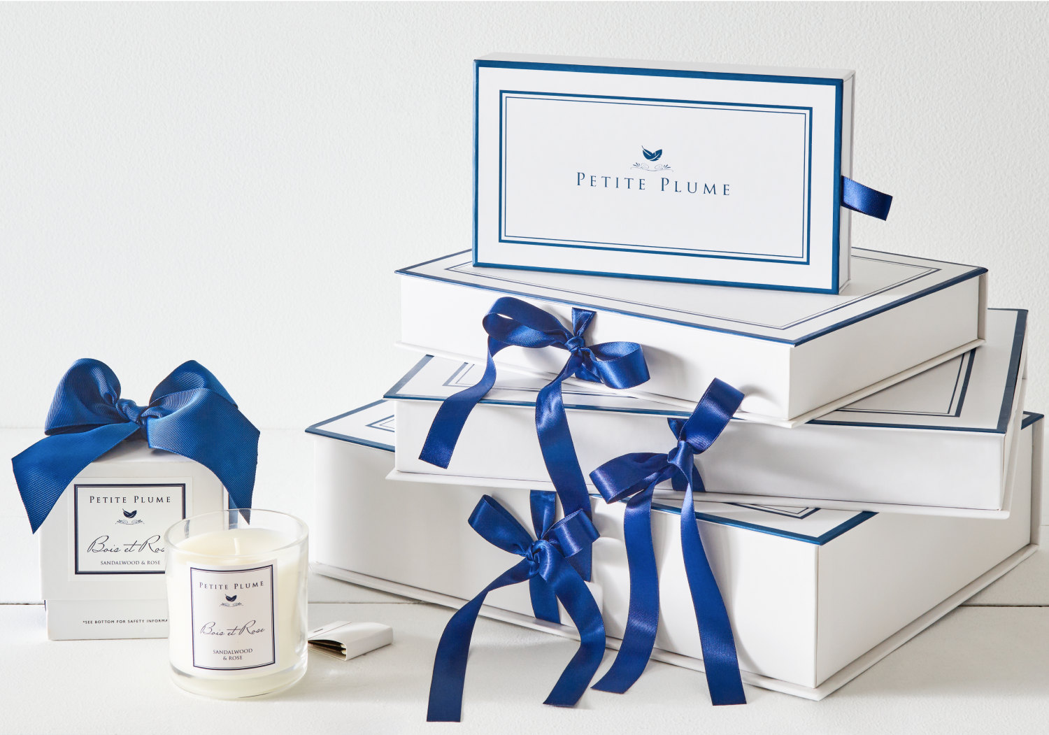 Stack of white and blue gift boxes with navy ribbons. To the left is a candle with matching gift box