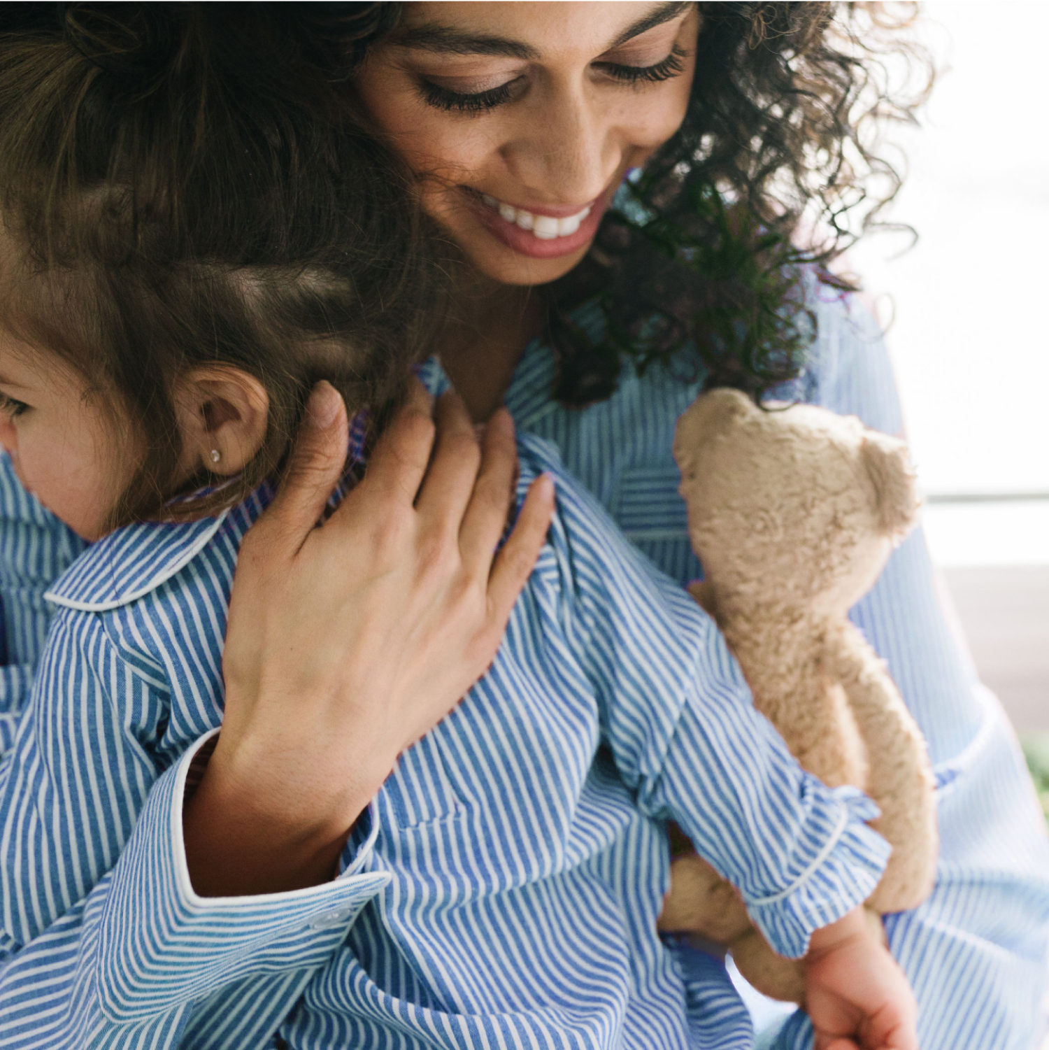 Mother embracing their young child in blue and white striped pajamas