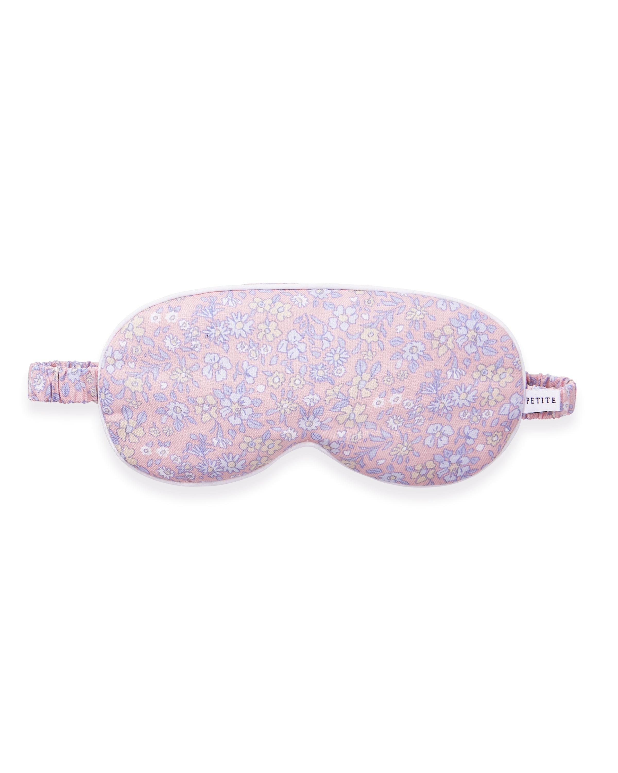 A woman with long brown hair wears the Adult's Twill Sleep Mask in Fleur Blush, lifting it slightly with one hand as she gazes off to the side with a relaxed expression.