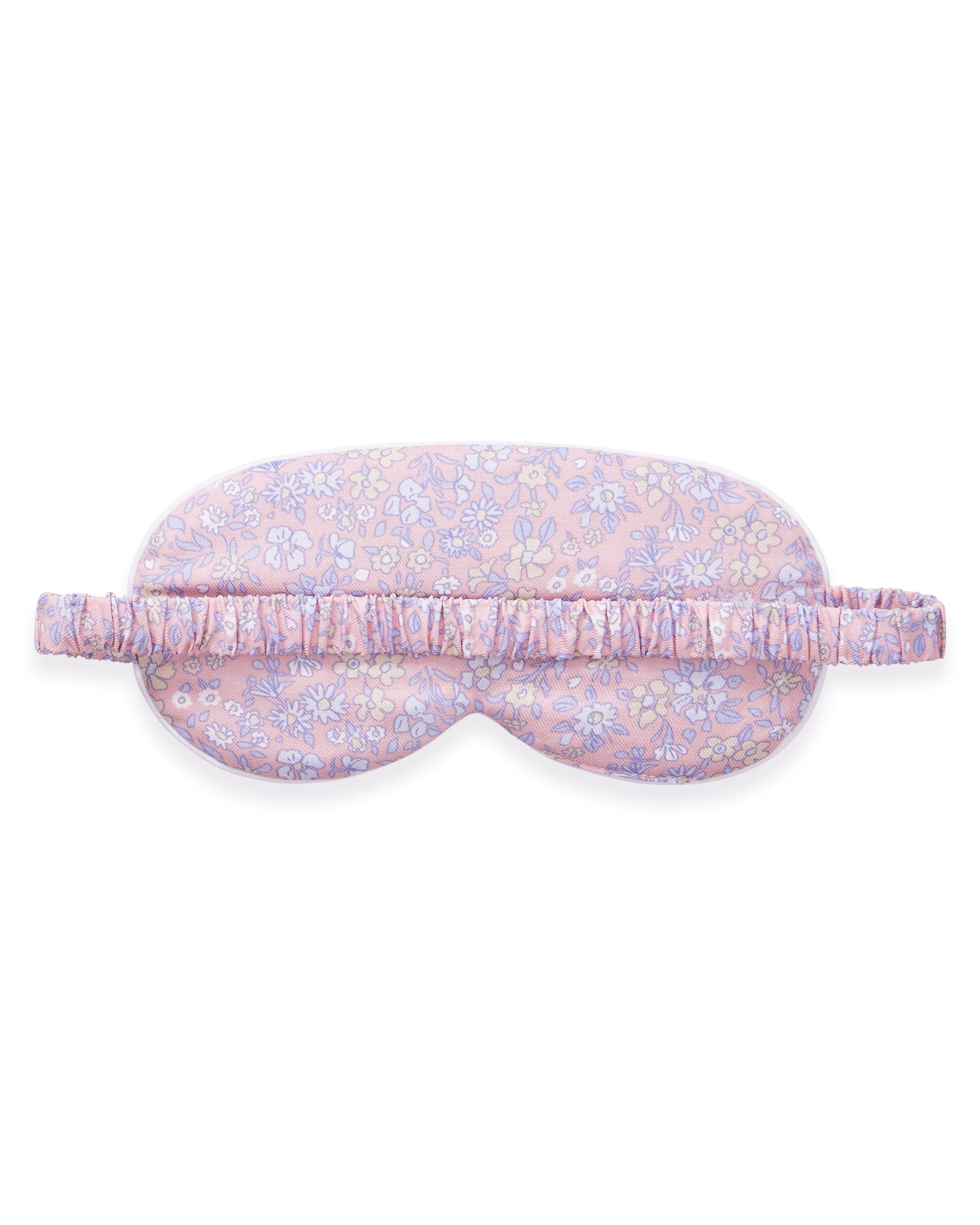 A woman with long brown hair wears the Adult's Twill Sleep Mask in Fleur Blush, lifting it slightly with one hand as she gazes off to the side with a relaxed expression.