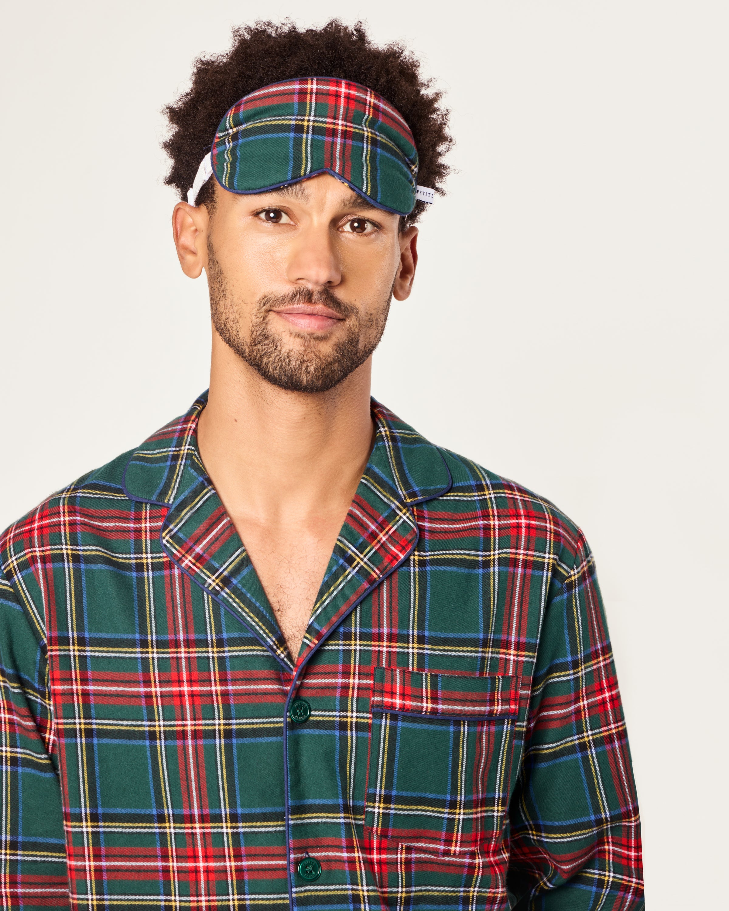 The Adult's Twill Sleep Mask in Kensington Tartan features a green, red, and blue plaid pattern, an elastic strap, and a small white side tag, shown against a white background.