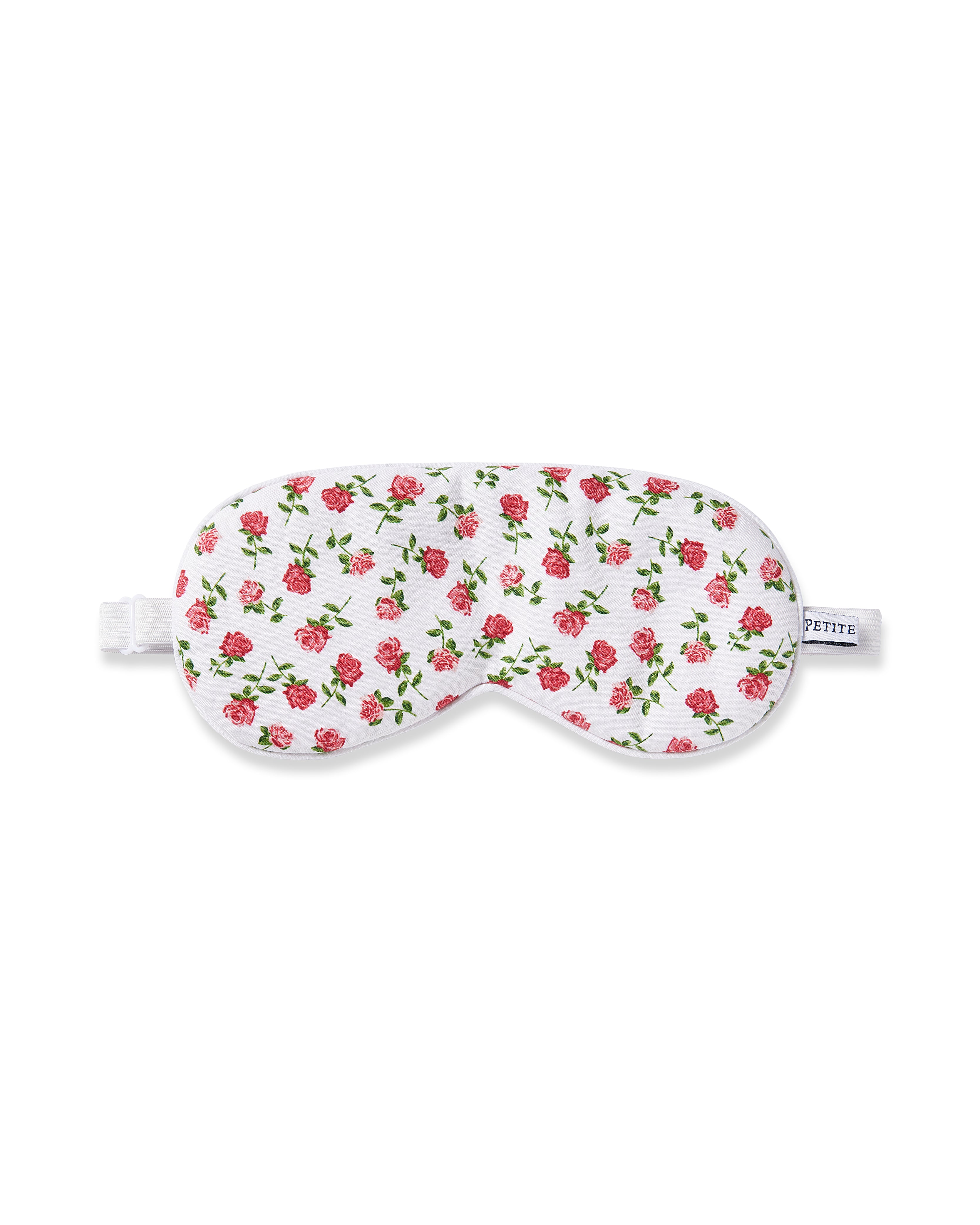 The Petite Plume Adults Twill Sleep Mask in Petite Petals features a white floral design with pink roses and green leaves. It includes an adjustable strap for comfort and a small side tag that can be monogrammed for a personalized touch.