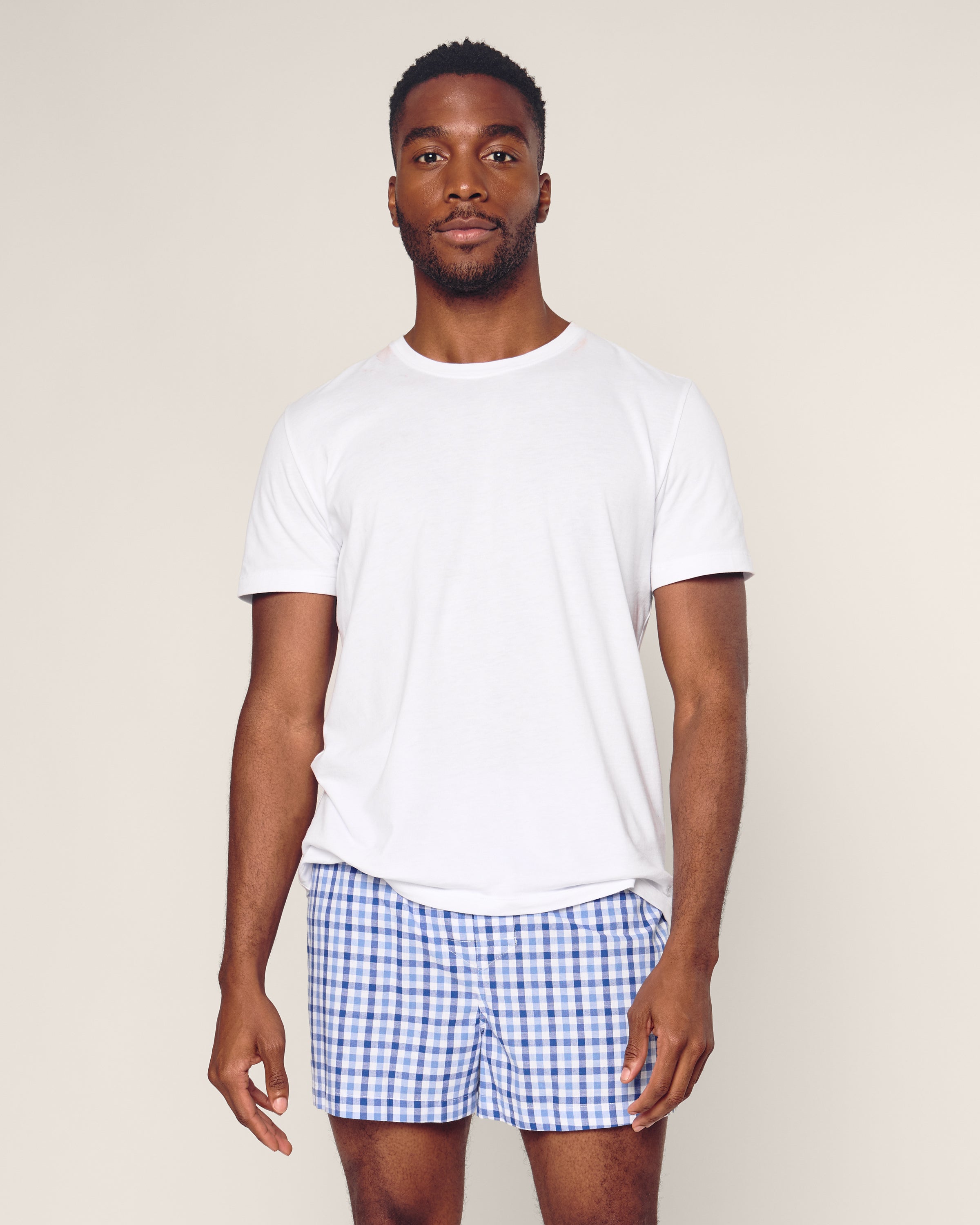 A man in a plain white t-shirt and Petite Plume’s Mens Twill Boxers in Royal Blue Gingham, made from woven cotton twill for a classic fit, stands against a neutral background.
