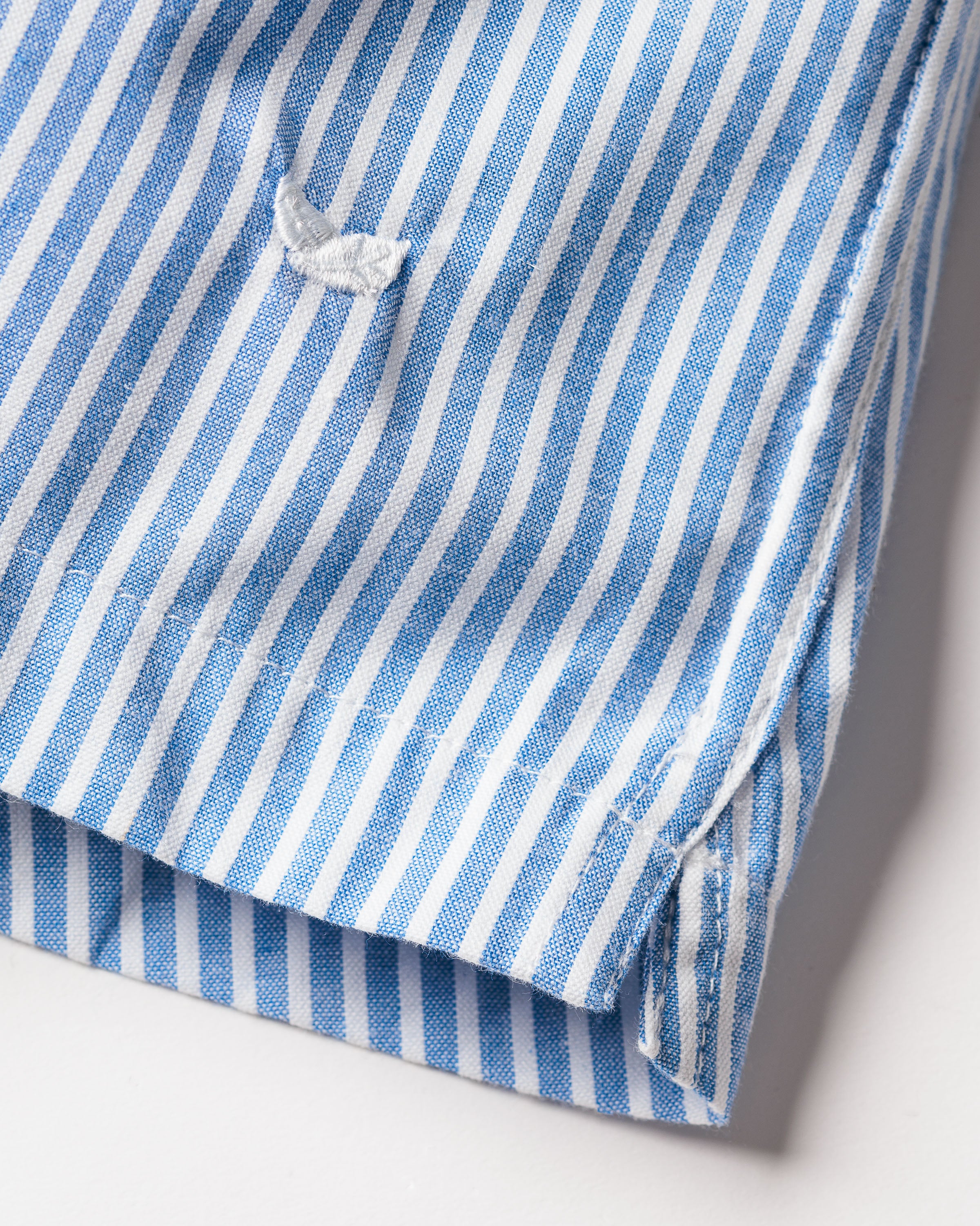 Close-up of a blue and white striped woven cotton twill fabric with a small embroidered detail in white. The edge is neatly finished, suggesting its from Petite Plumes classic fit Mens Twill 3 Pack Boxers in Royal Blue Gingham.